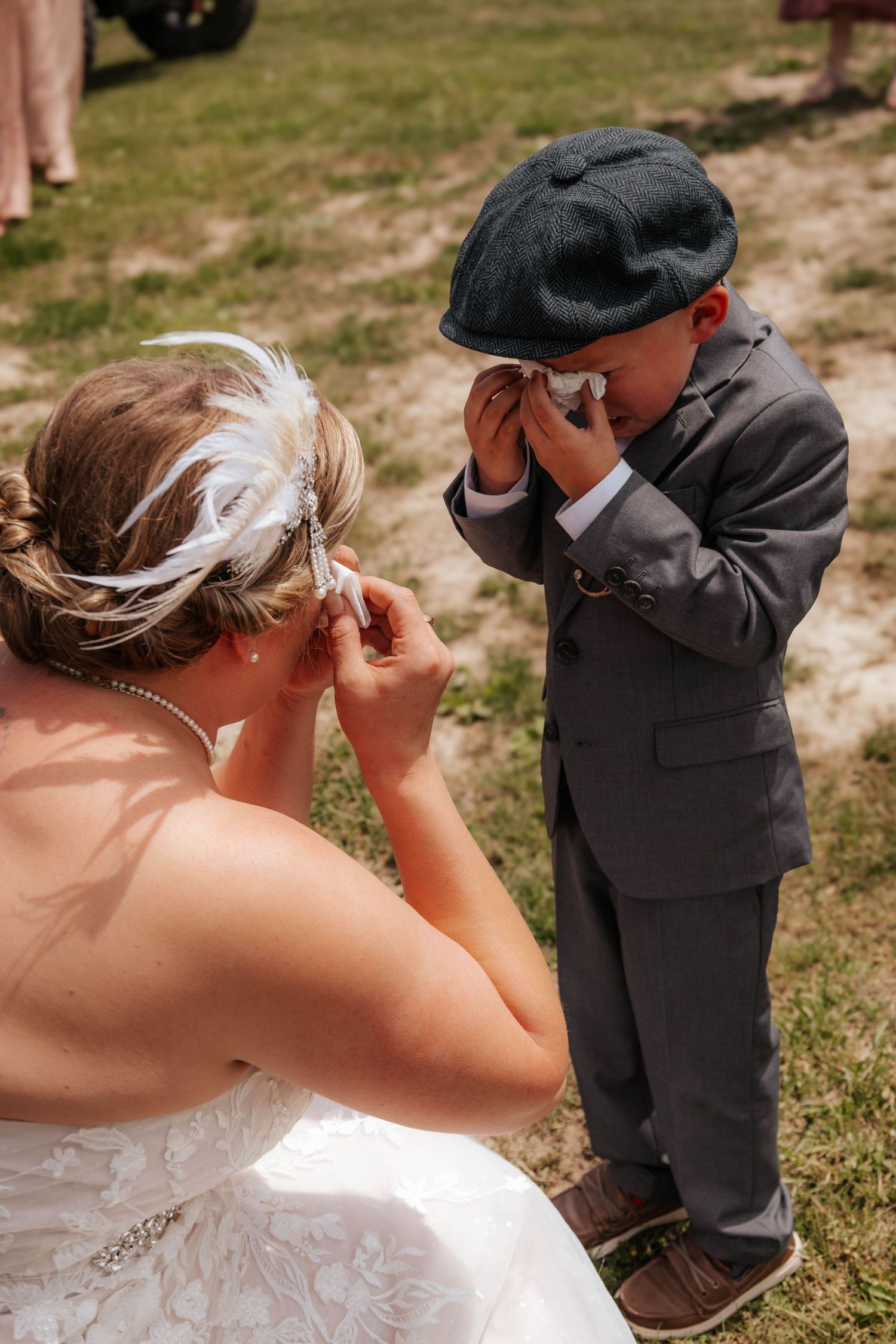 Touching moment of a bride and small child in formal attire wiping tears at outdoor wedding.