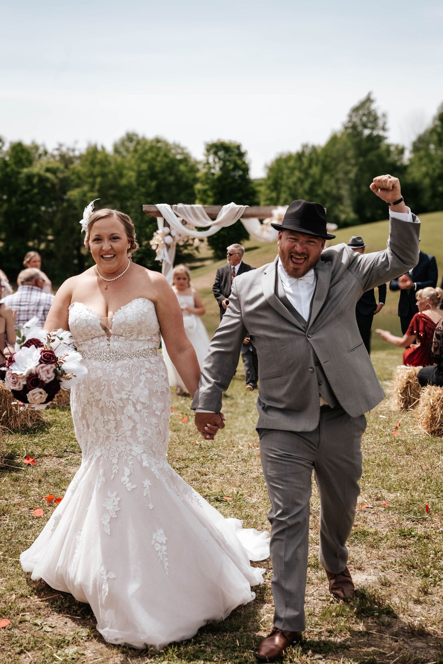 Joyful newlyweds celebrating while walking down the aisle at outdoor countryside wedding.