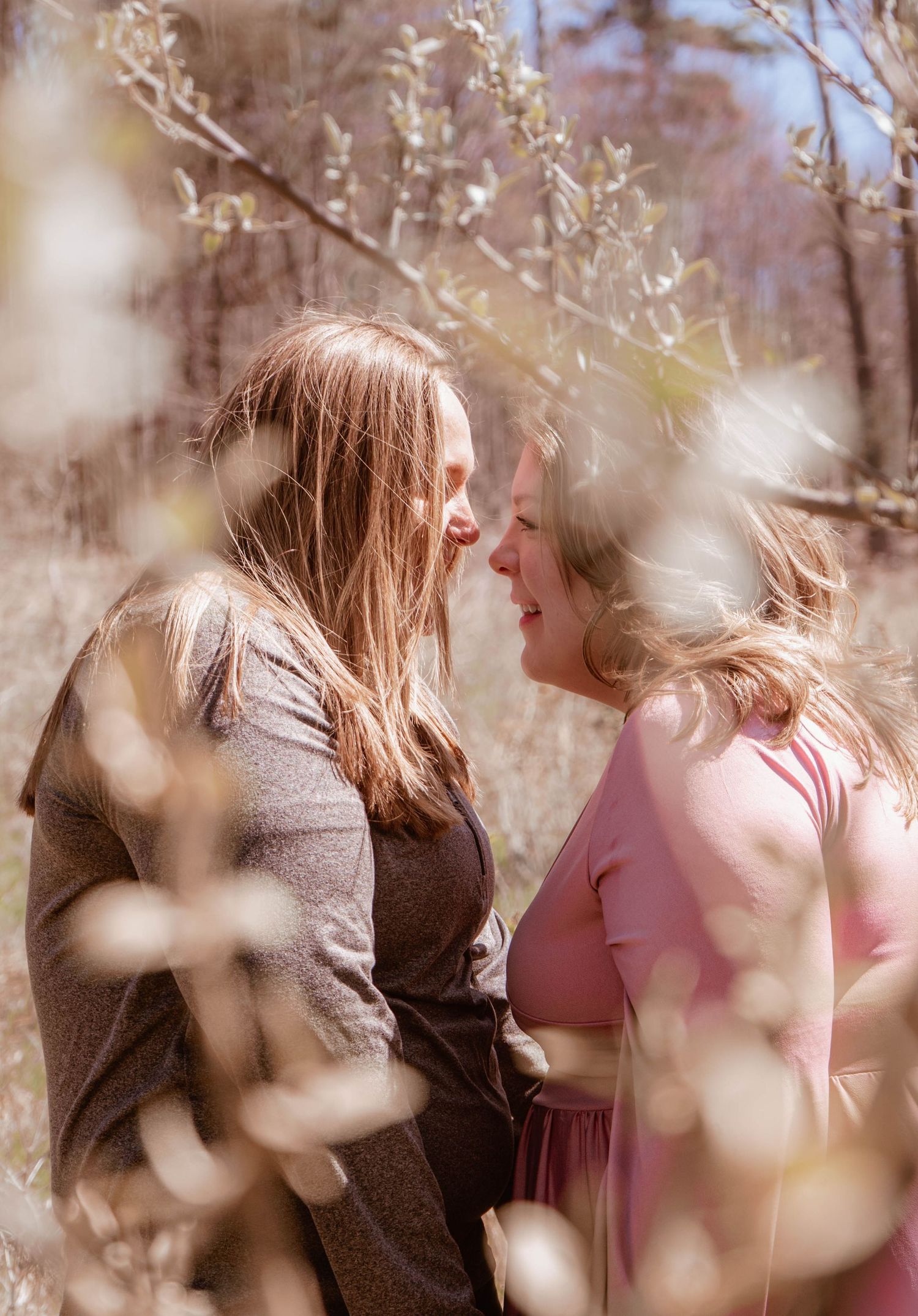 Two people share a tender moment among blooming spring branches with soft sunlight filtering through the trees.
