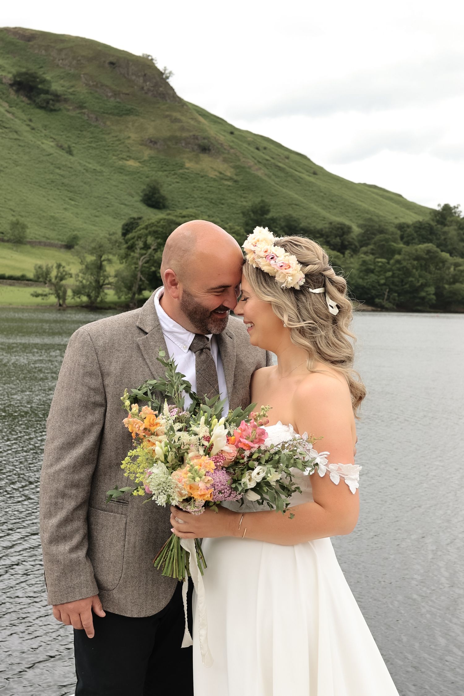 A couple shares an intimate moment by a lake with mountains in the background.
