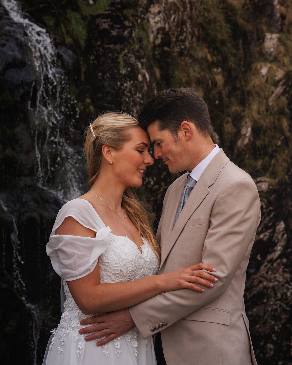 A romantic waterfall wedding portrait with couple embracing in soft lighting.