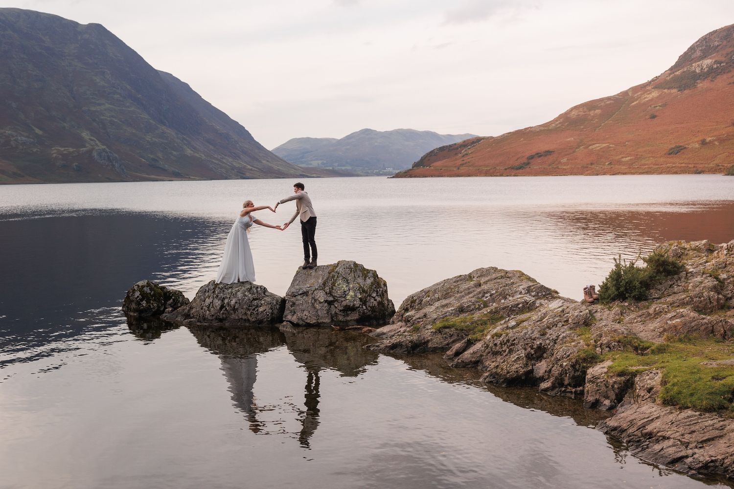 A romantic lakeside scene with silhouettes standing on rocks against a backdrop of misty mountains at a Scottish loch.