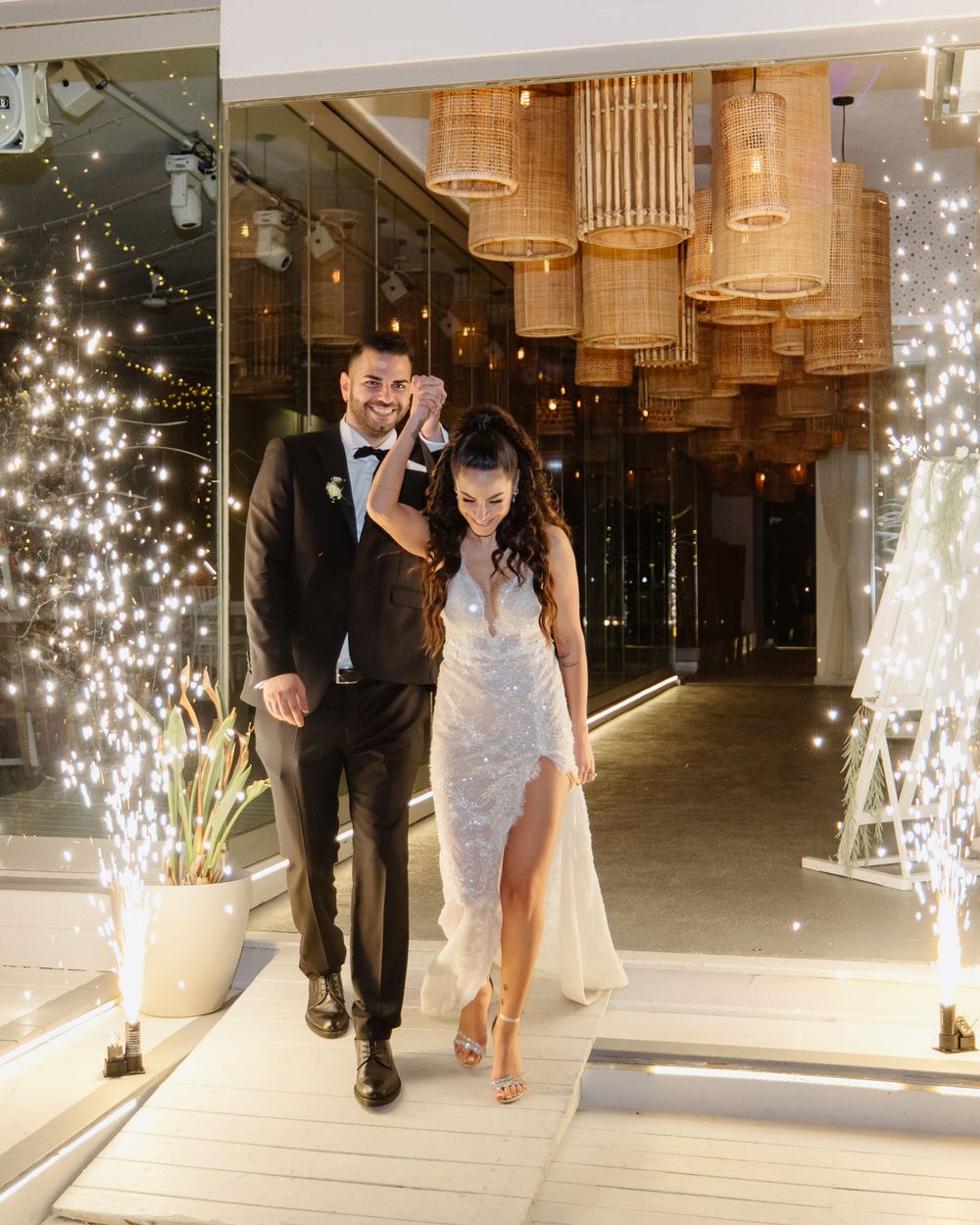 Bride and groom make a grand entrance at Galu Seaside, walking through sparkler fountains with joyful smiles and elegant style.