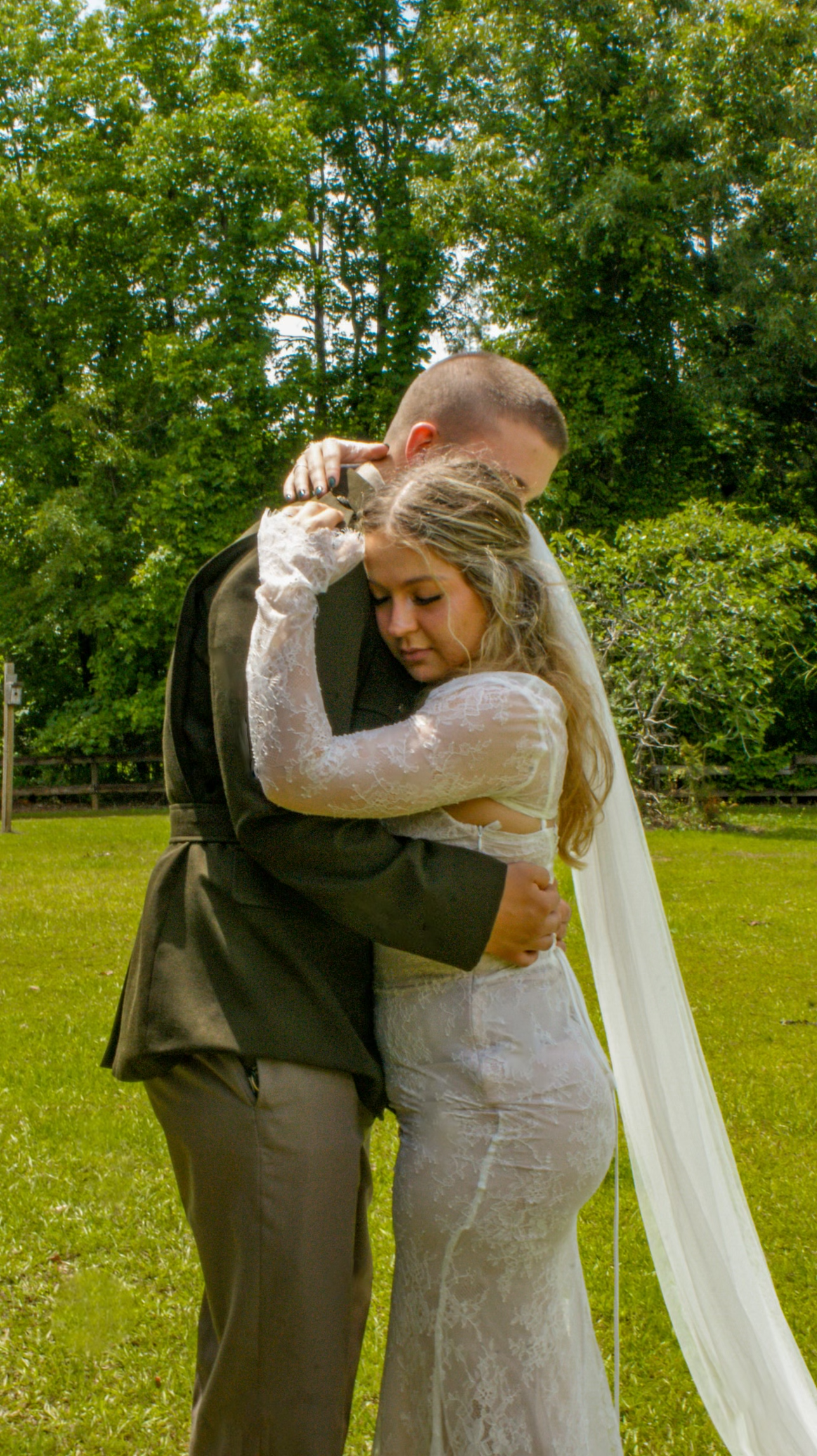 A newlywed couple embracing in a sunny garden, bride wearing a lace dress with flowing veil.