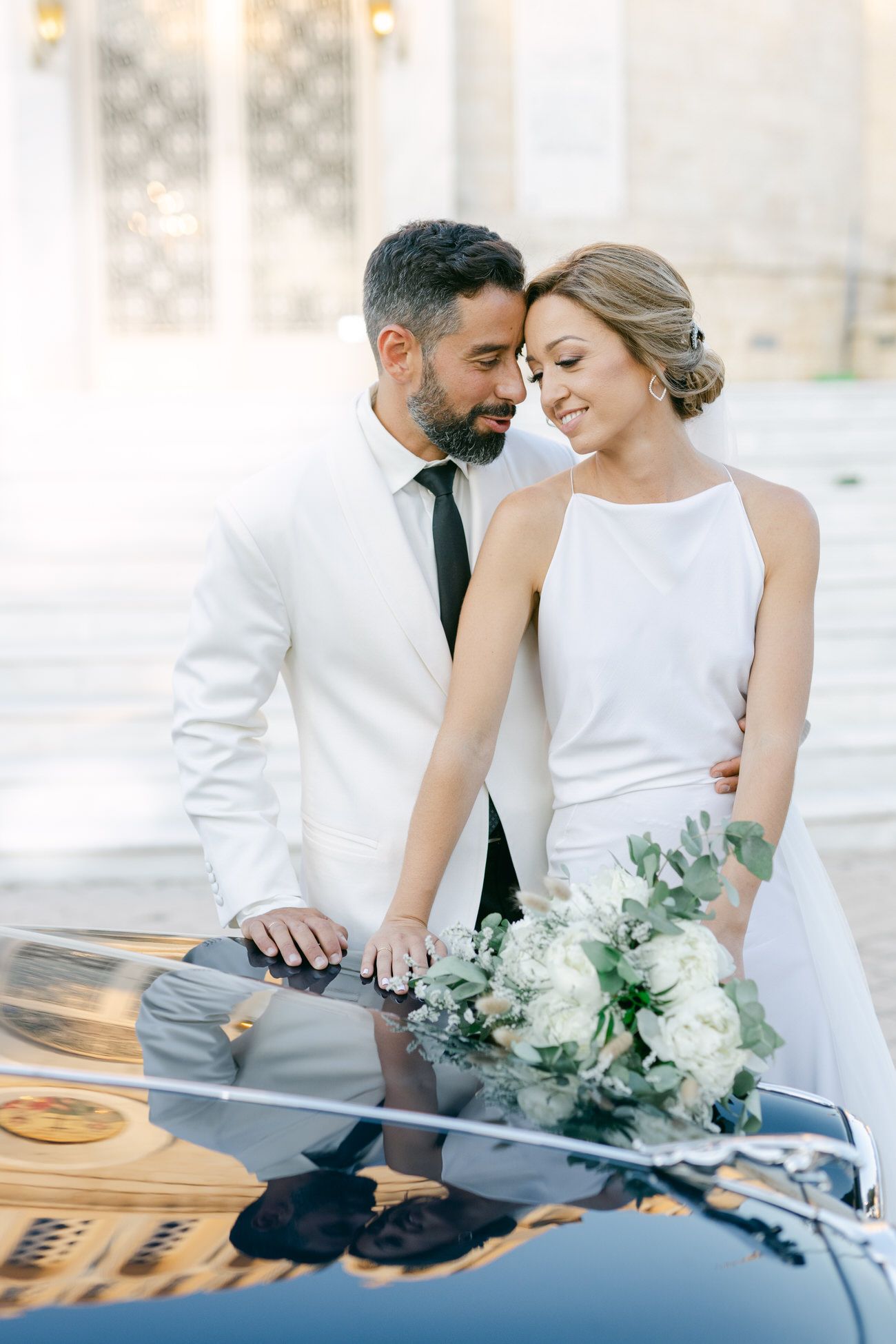 Elegant couple poses by vintage car with white floral bouquet on their wedding day. γαμος 2026