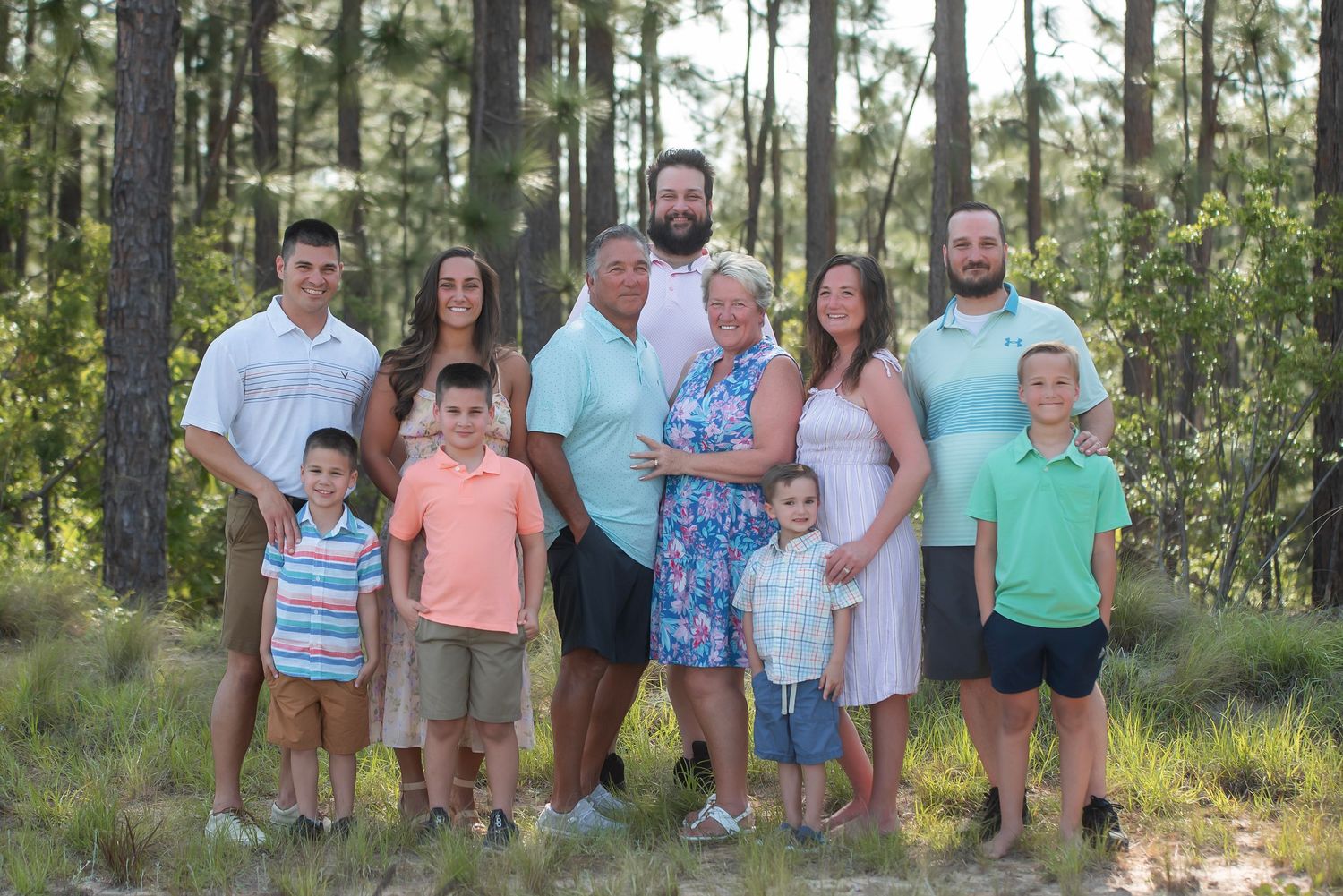 Extended family gathering for professional portraits in a pine forest setting.