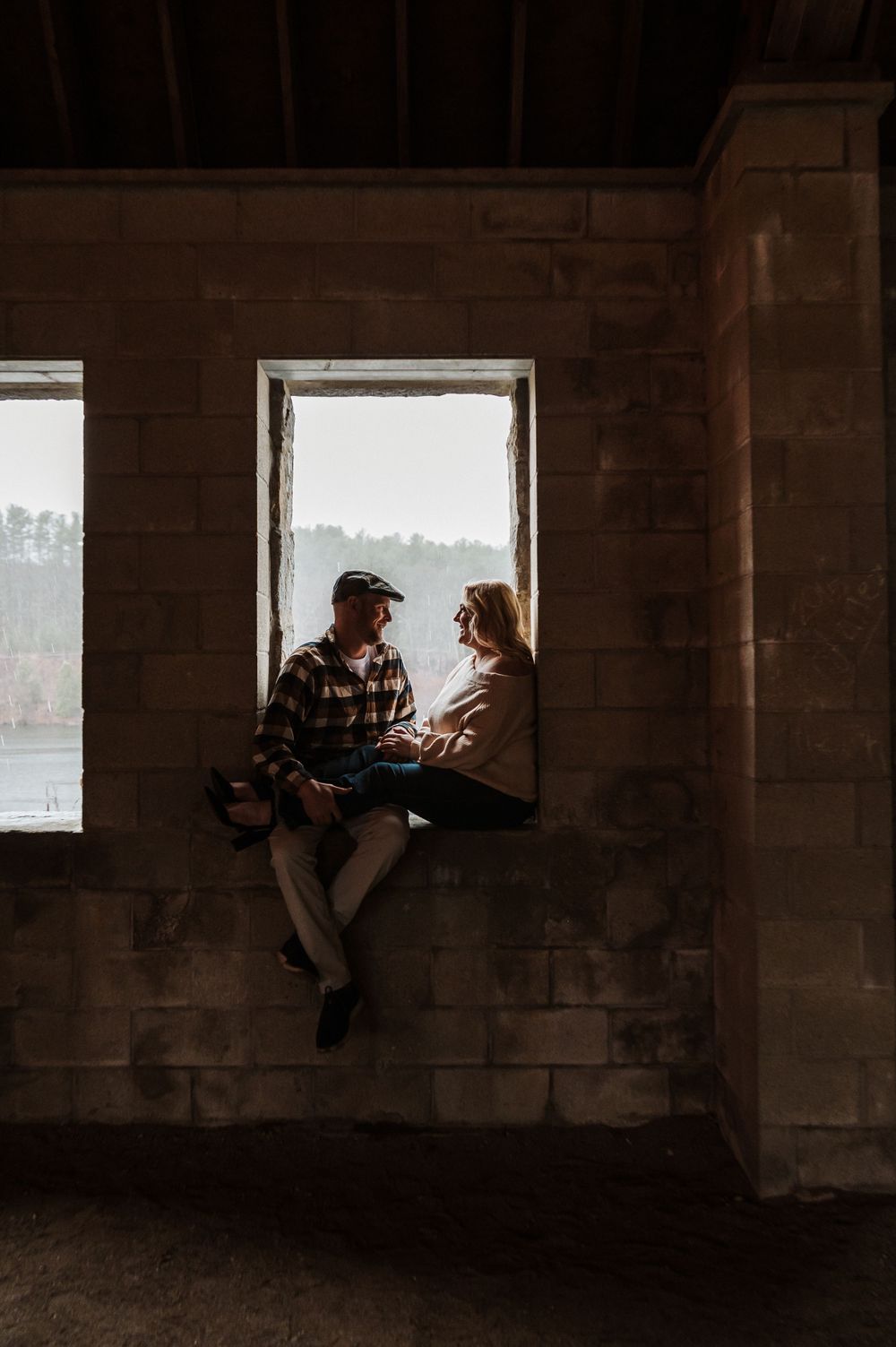 Two people sitting in silhouette on a window ledge having a conversation in an abandoned concrete building.