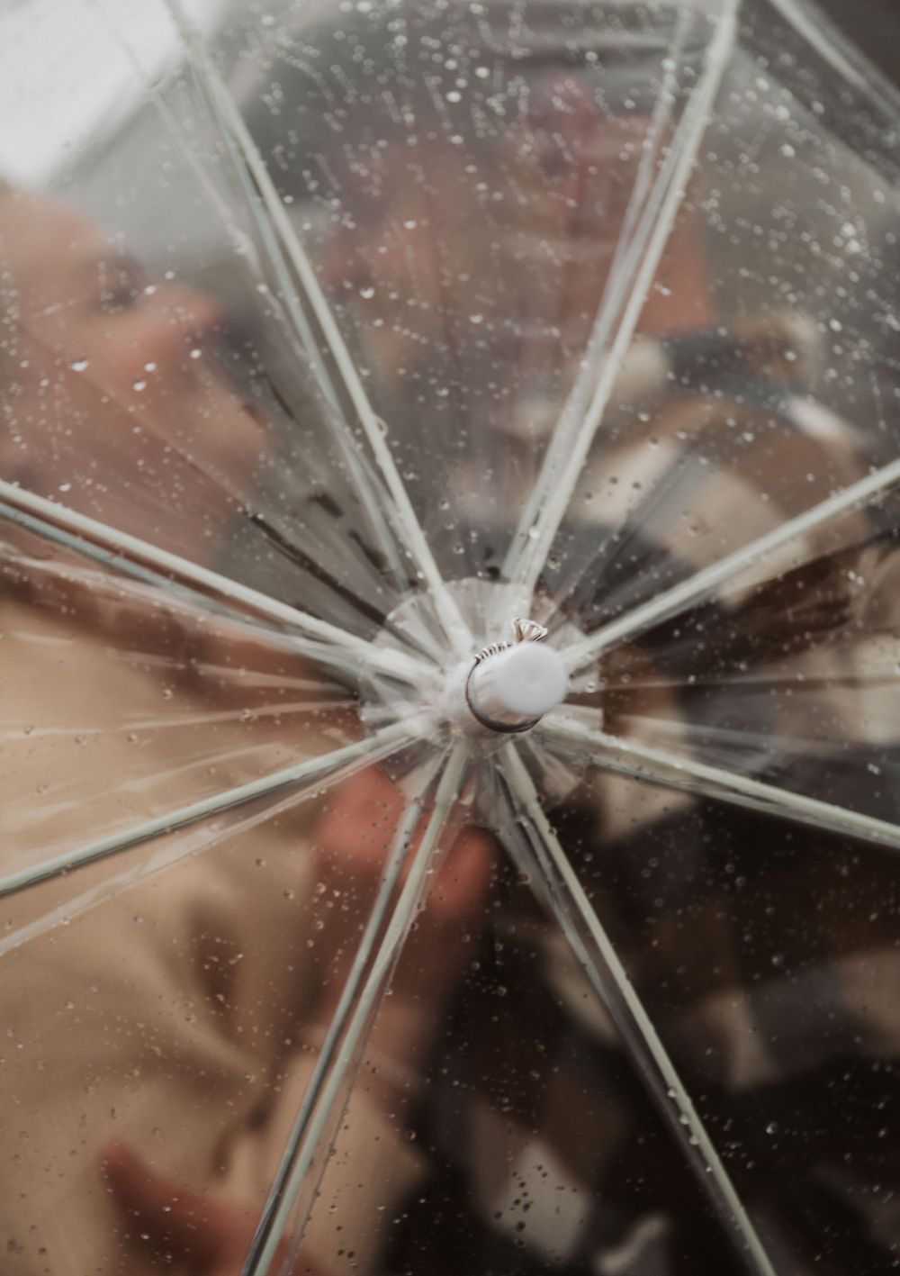 Close-up view of a transparent umbrella's center point with water droplets visible against a blurred background.