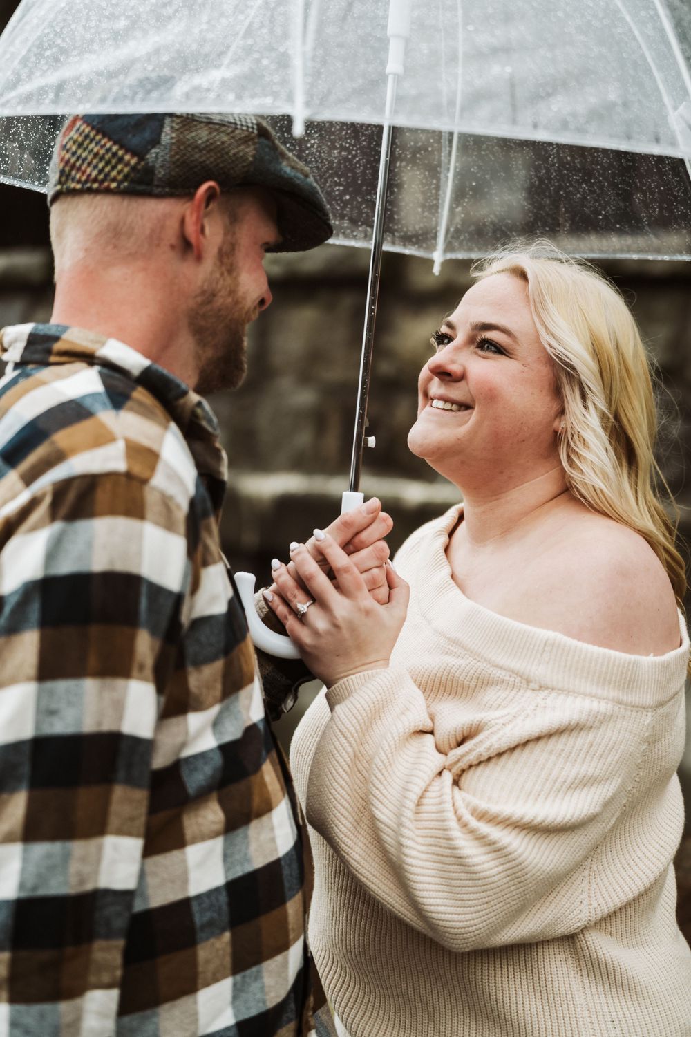 A couple shares a joyful moment together under a clear umbrella on a rainy day.
