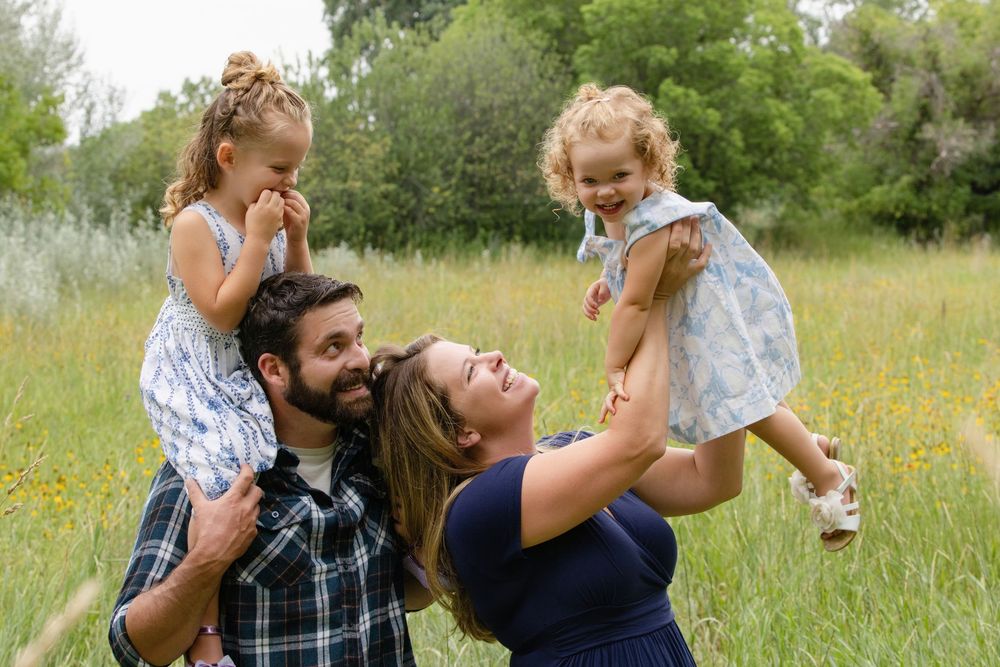 Four family members share a joyful moment together in a sunny meadow during summer.