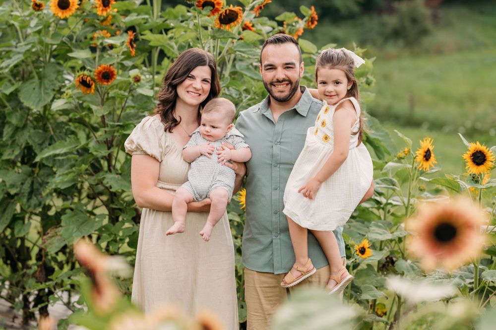 A family poses together in a beautiful sunflower garden on a sunny summer day.