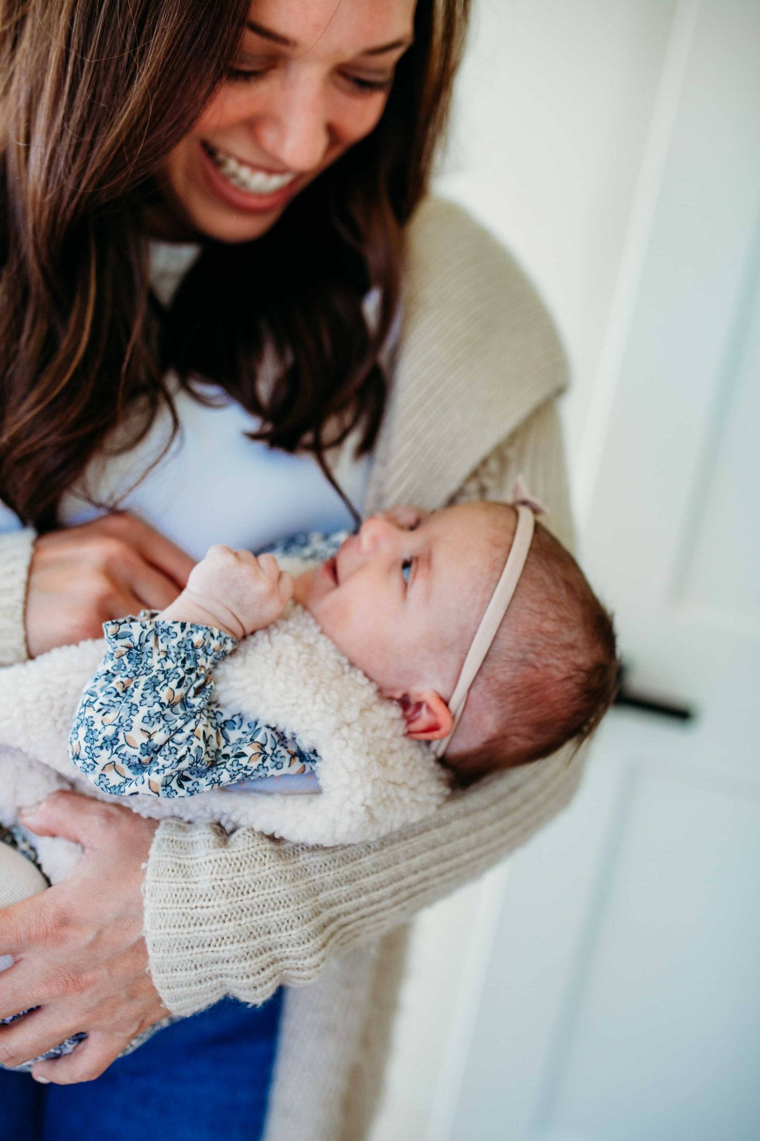 A baby wearing a blue and white outfit is being cradled in a knit sweater while gazing upward.
