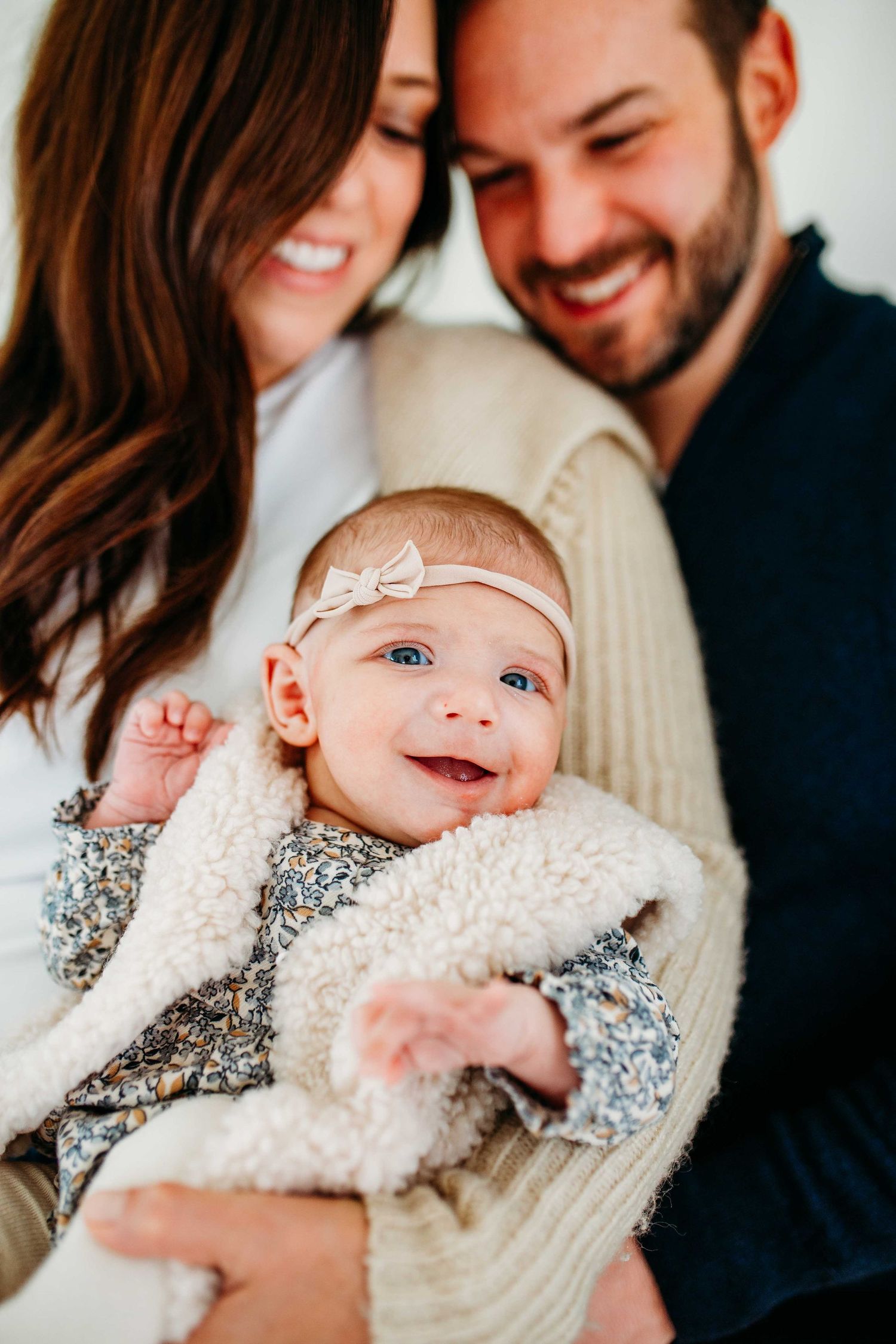 A happy family smiles and cuddles with a baby wearing a floral dress in this heartwarming portrait series.
