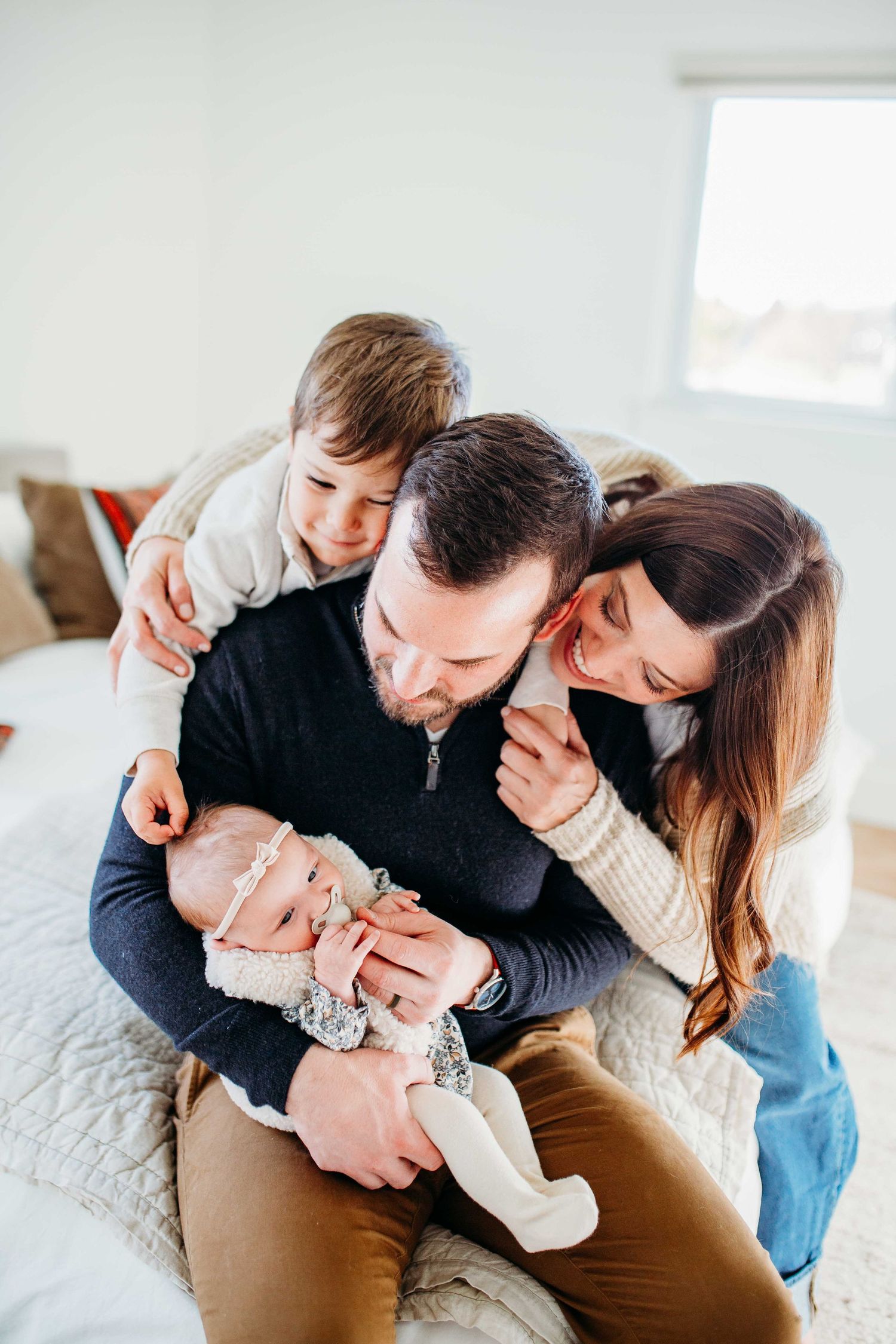 Parents cuddle and interact lovingly with their infant baby in a bright indoor setting during a lifestyle photoshoot.