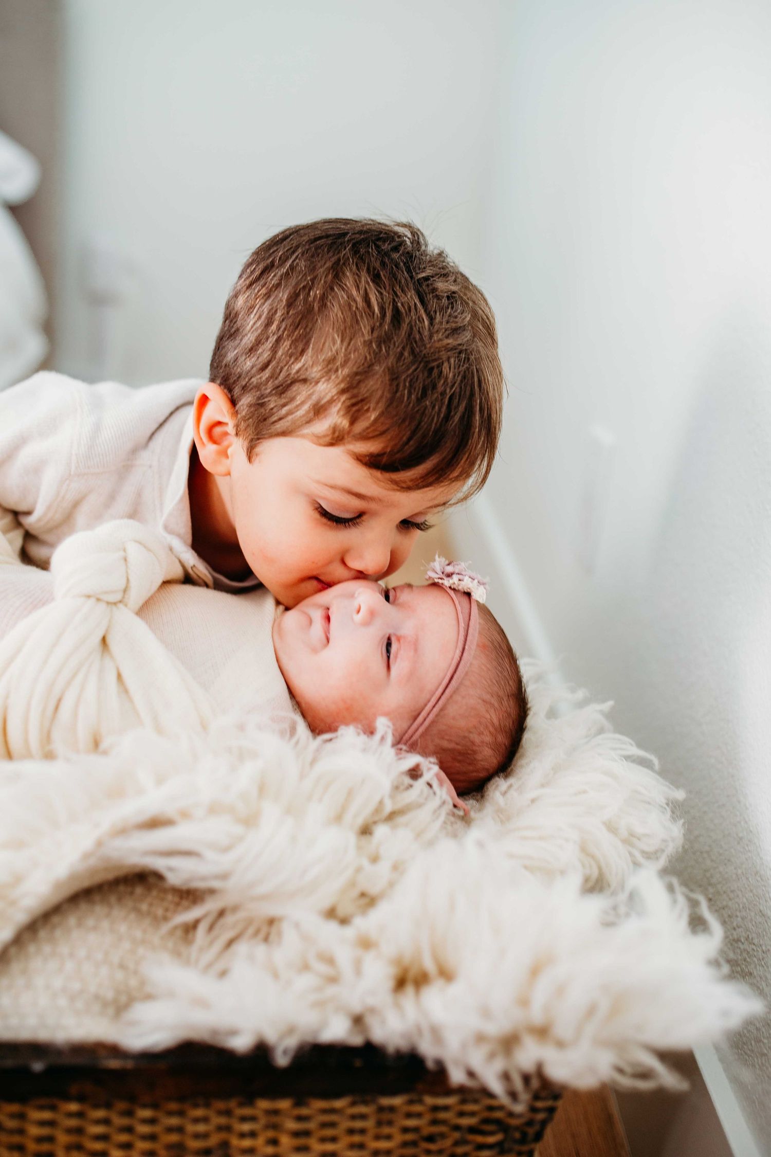 Two children sharing a sweet moment on a fluffy white fur blanket in a natural light setting.