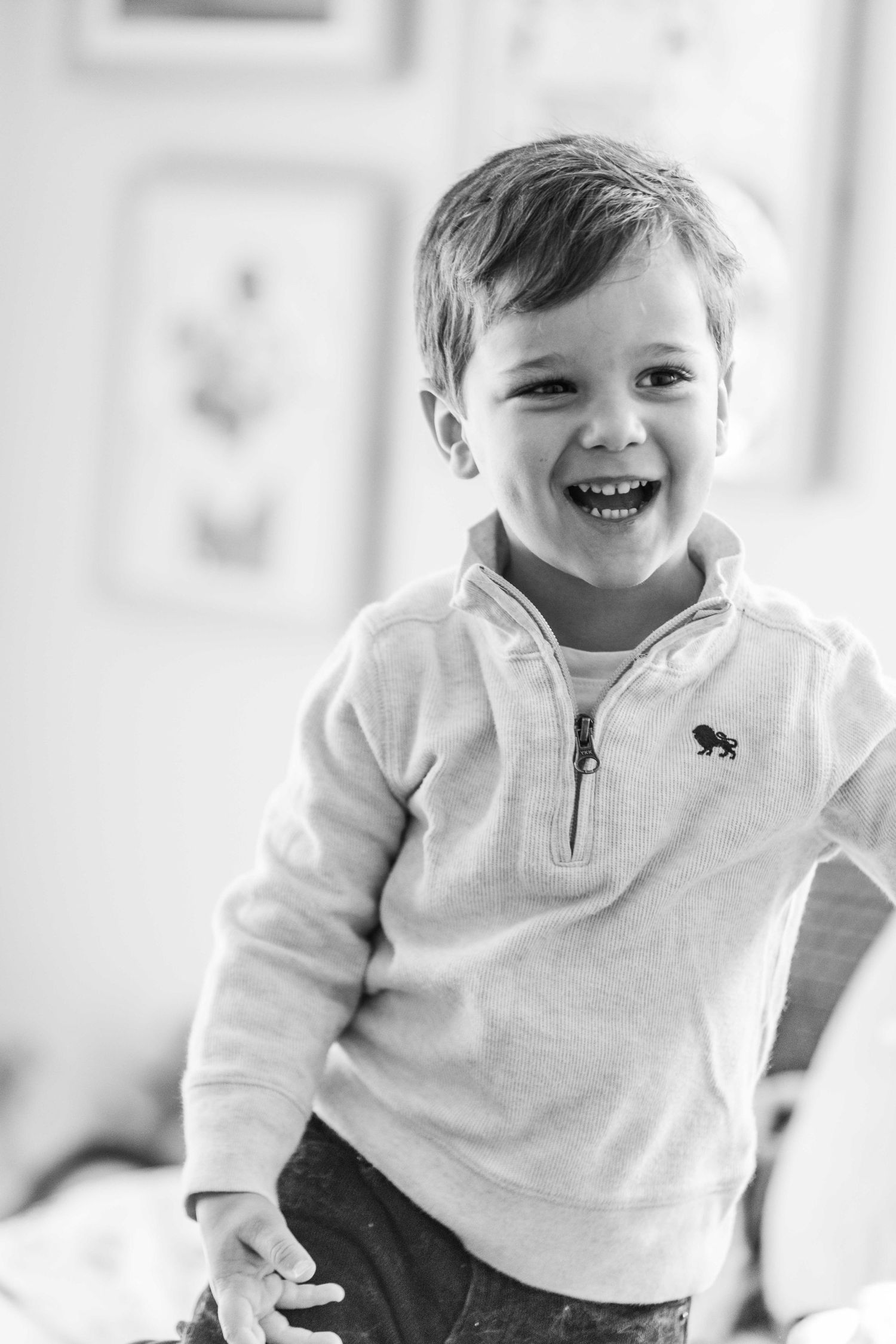 Black and white portrait of a young child wearing a white quarter-zip pullover smiling joyfully at the camera.