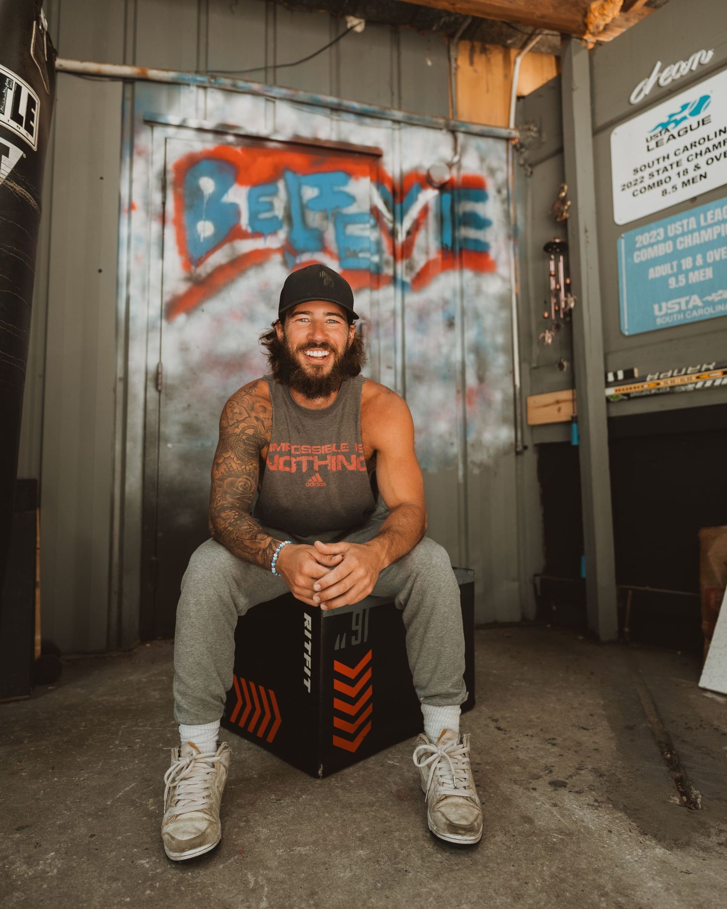 Someone in casual athletic wear sits on a storage container against a wall with graffiti in an urban setting.