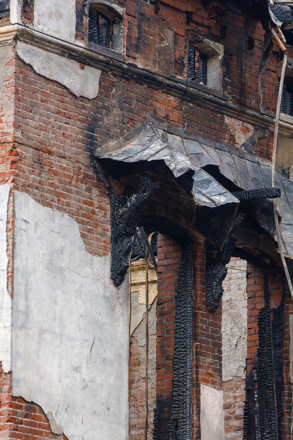 Charred and deteriorating brick facade of an old building with damaged black metal awning and exposed architectural details.