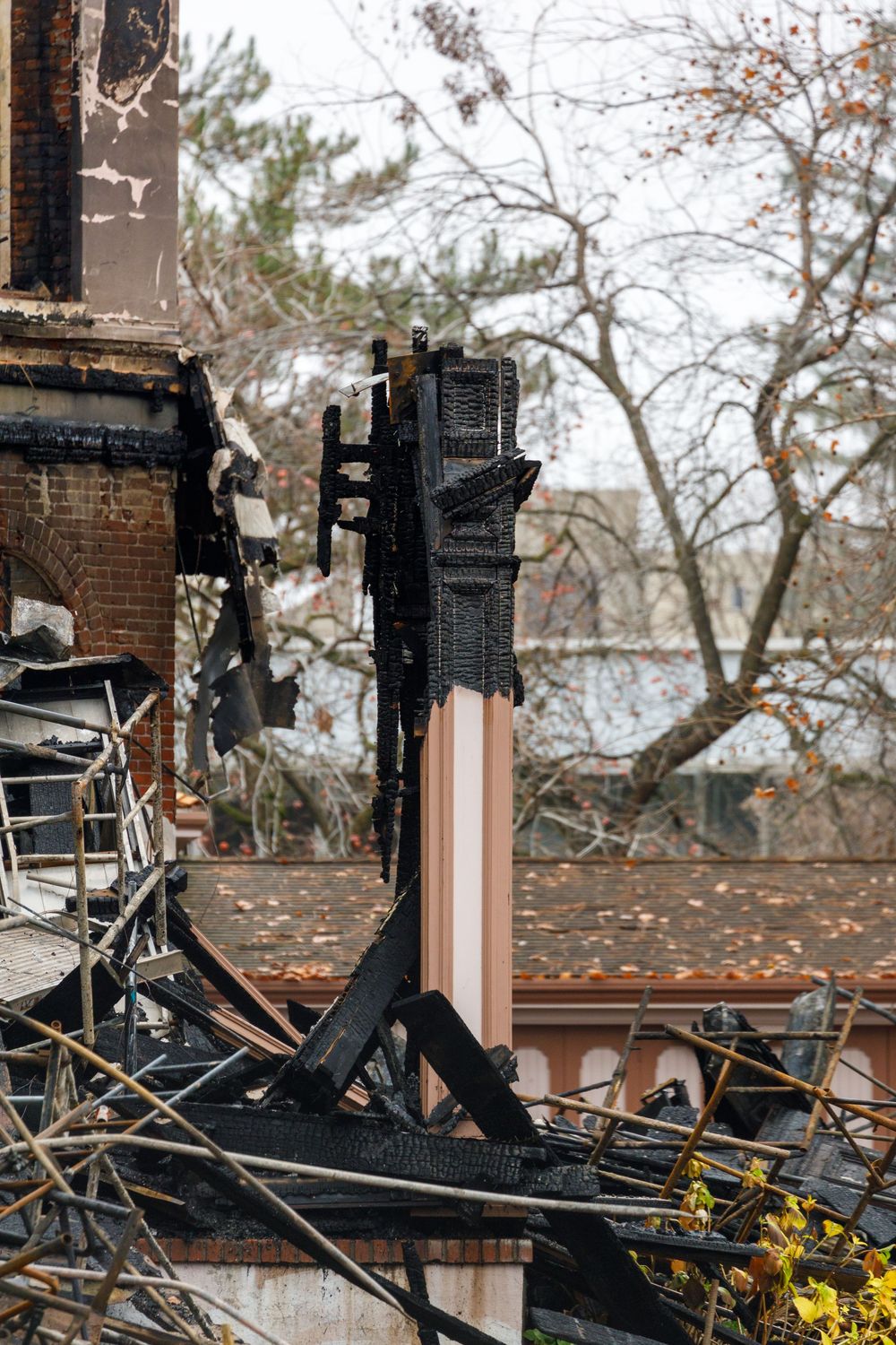 Charred wooden beams and structural damage show the aftermath of a house fire with bare trees in the background.