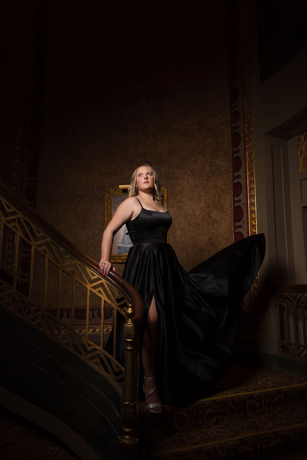 Dramatic shot of a flowing black dress in motion on an ornate staircase with moody lighting and vintage backdrop.