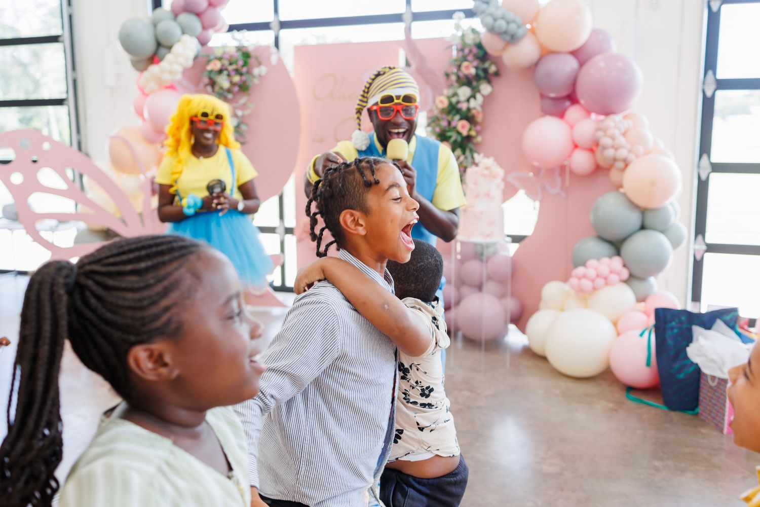 A festive party scene with balloons and decorations featuring people dancing and celebrating against a pink balloon arch backdrop.