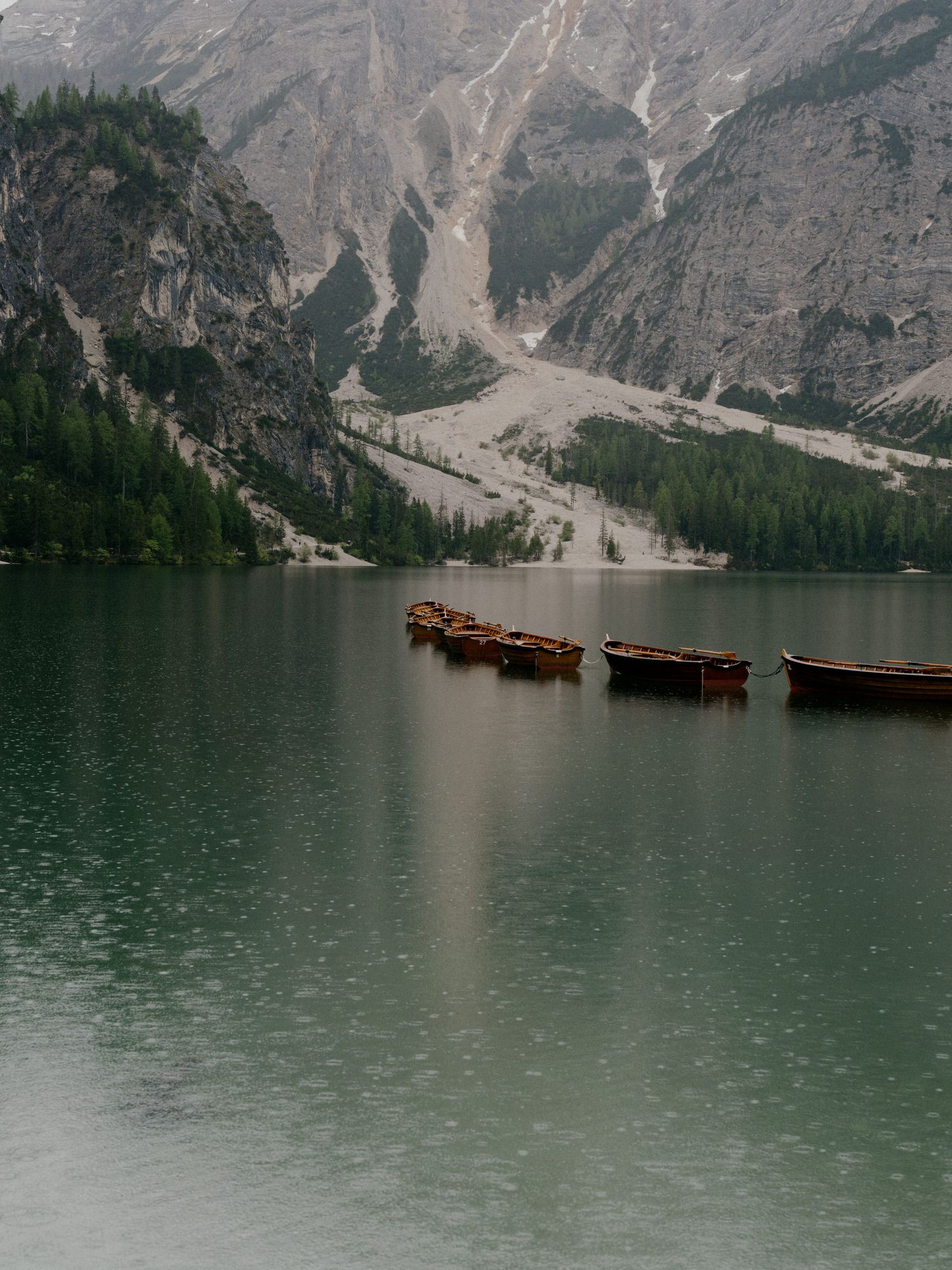 Wooden docks and boats on a misty mountain lake surrounded by towering peaks and evergreen forest in the Dolomites.