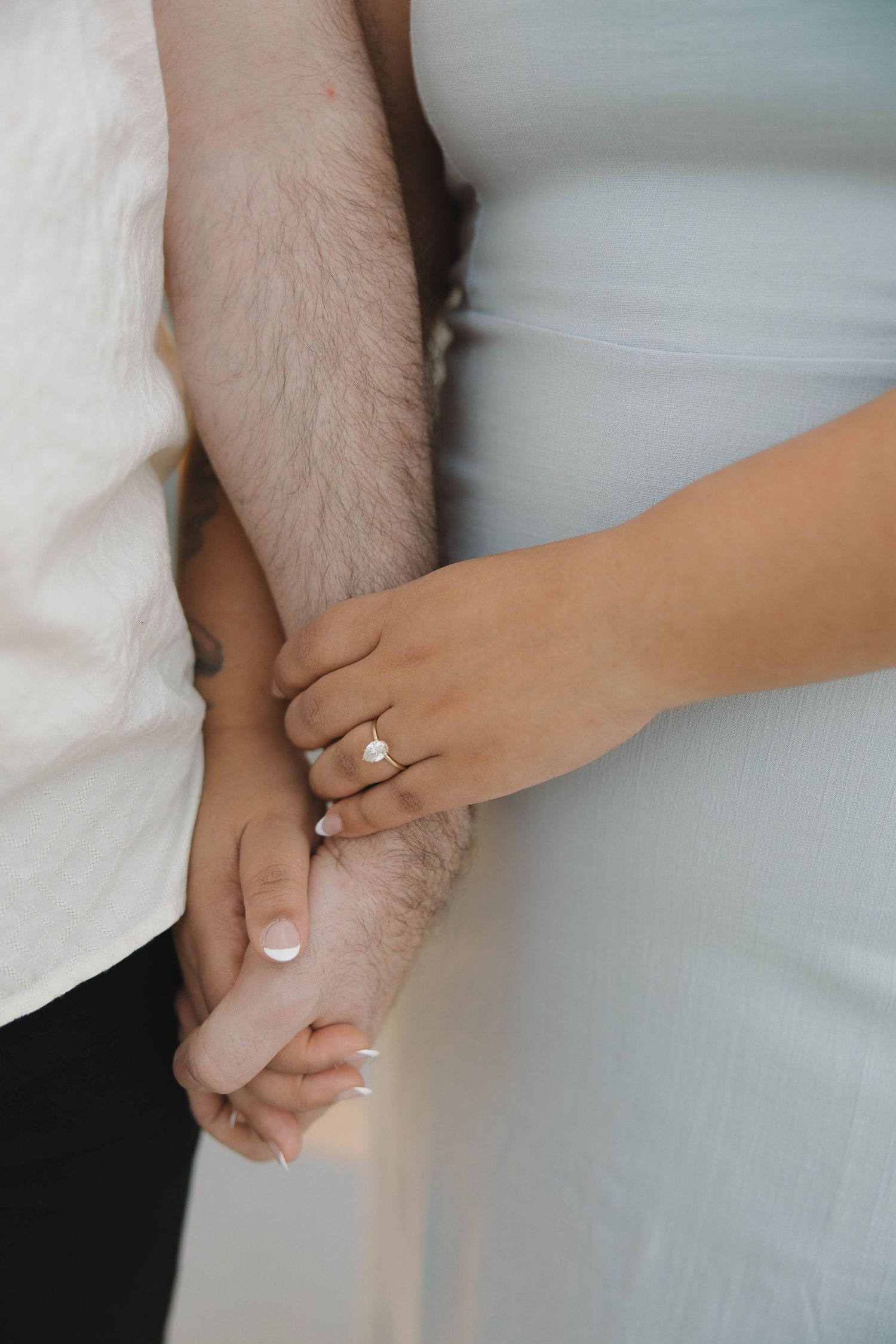 Close-up of couple holding hands with engagement ring visible in elegant white and grey tones.