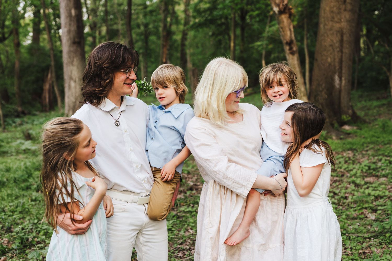 A group dressed in coordinating white and light blue outfits stands together in a peaceful wooded setting.
