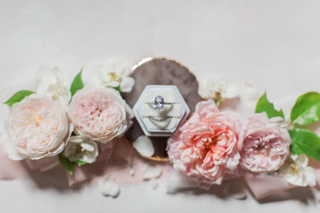Wedding ring and large diamond engagement ring displayed elegantly among soft pink garden roses on light textured surface. Oxfordshire