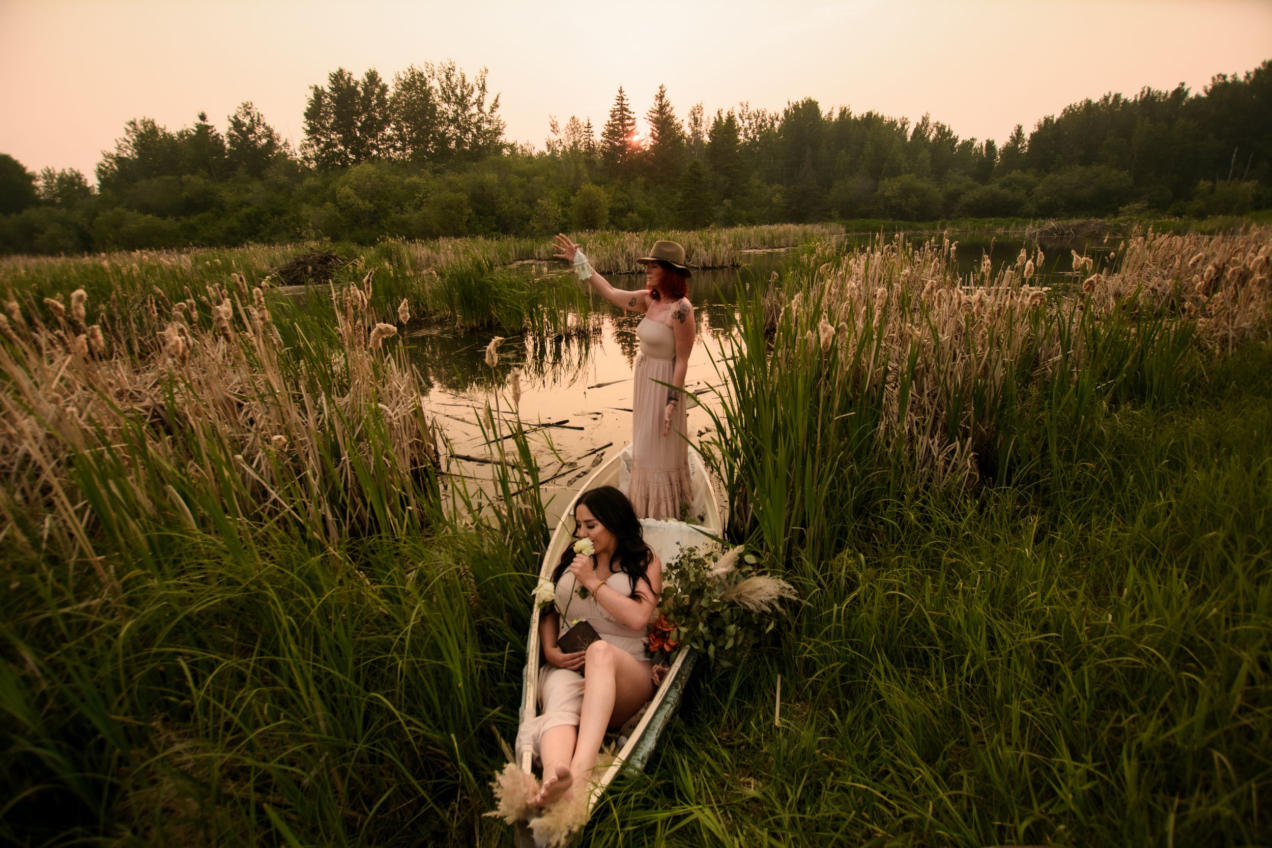 A person relaxes in a vintage rowboat among tall reeds at sunset on a serene lake.