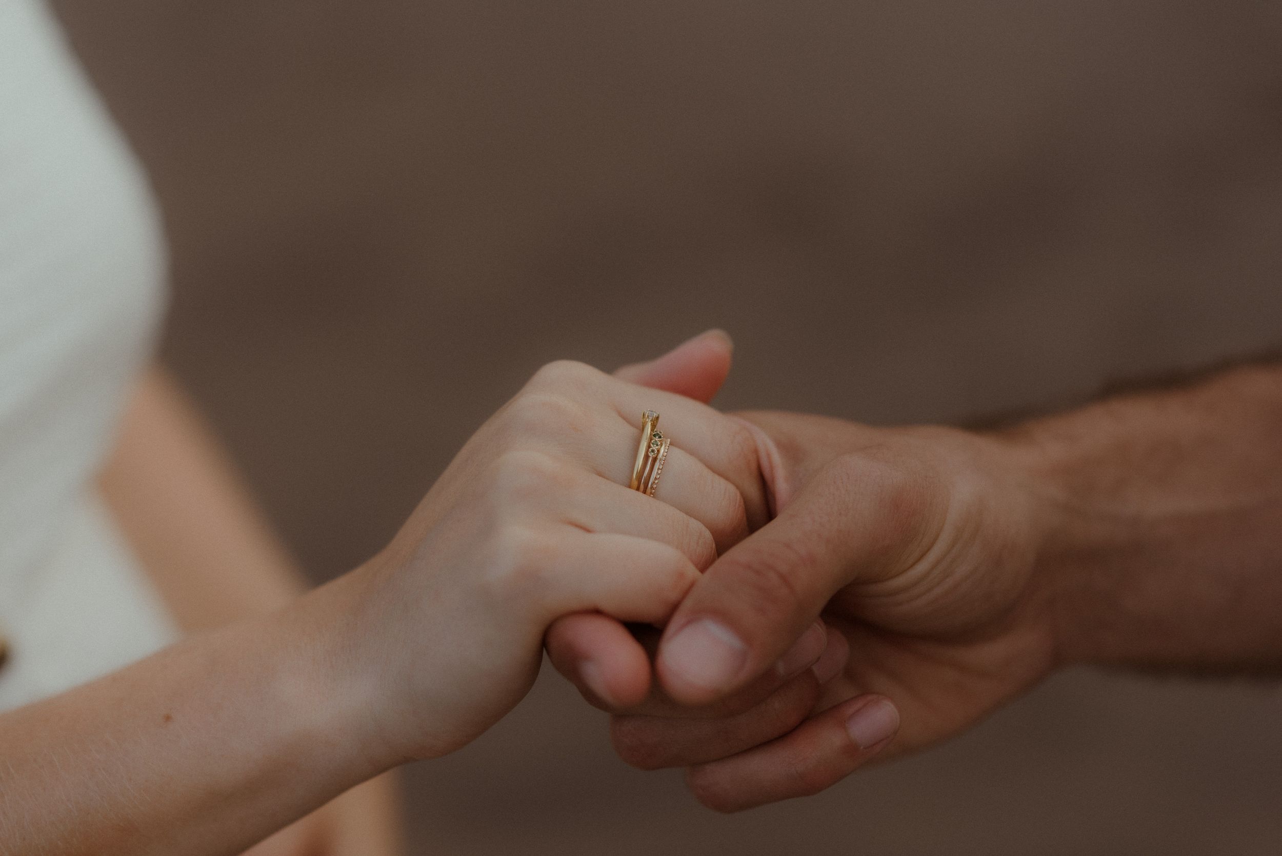 Close up of two hands gently holding each other against a blurred brown background in El Médano, Tenerife.