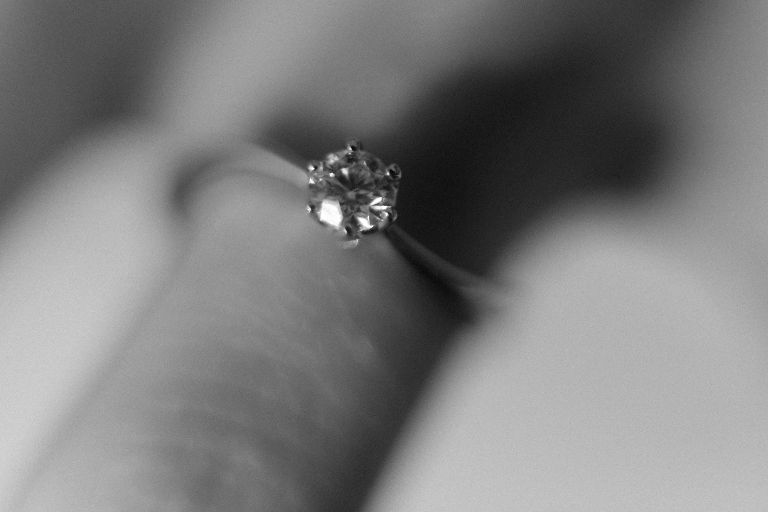 Close-up black and white photograph of a single diamond engagement ring with shallow depth of field.