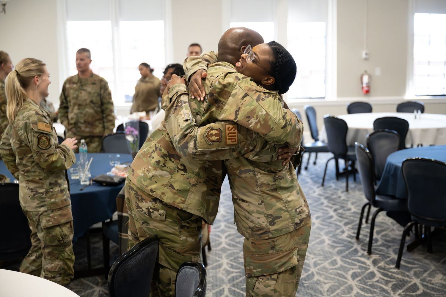 Service members share emotional embrace during military gathering in conference room.