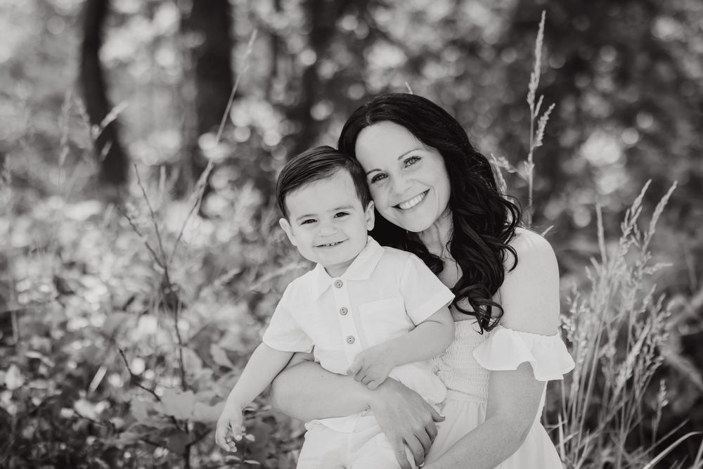 Black and white photo of mother and baby sitting amongst wildflowers in a natural outdoor setting.