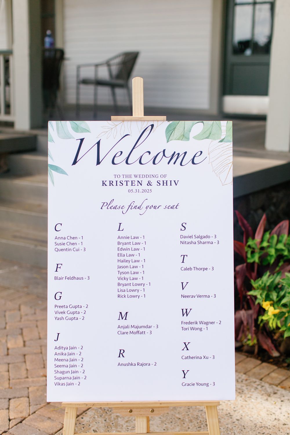 An elegant wedding seating chart with 'Welcome' text displayed on a white easel with watercolor greenery details.