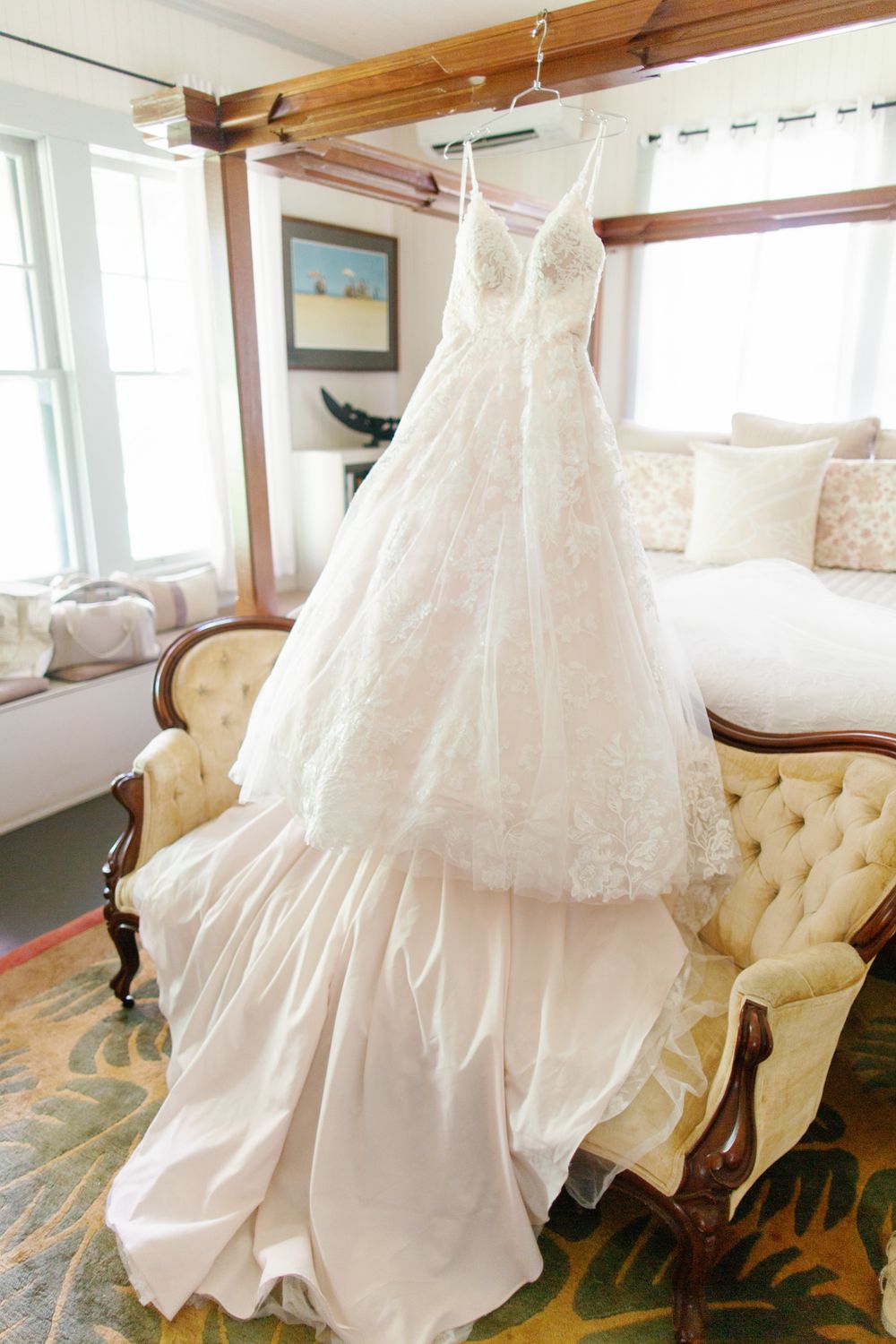 An elegant white wedding dress with lace details and flowing layers hangs gracefully on display in a sunlit room.