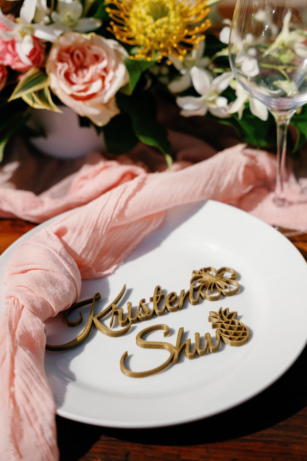 Elegant white place setting with gold lettering and pink floral decorations on a dark wooden surface.