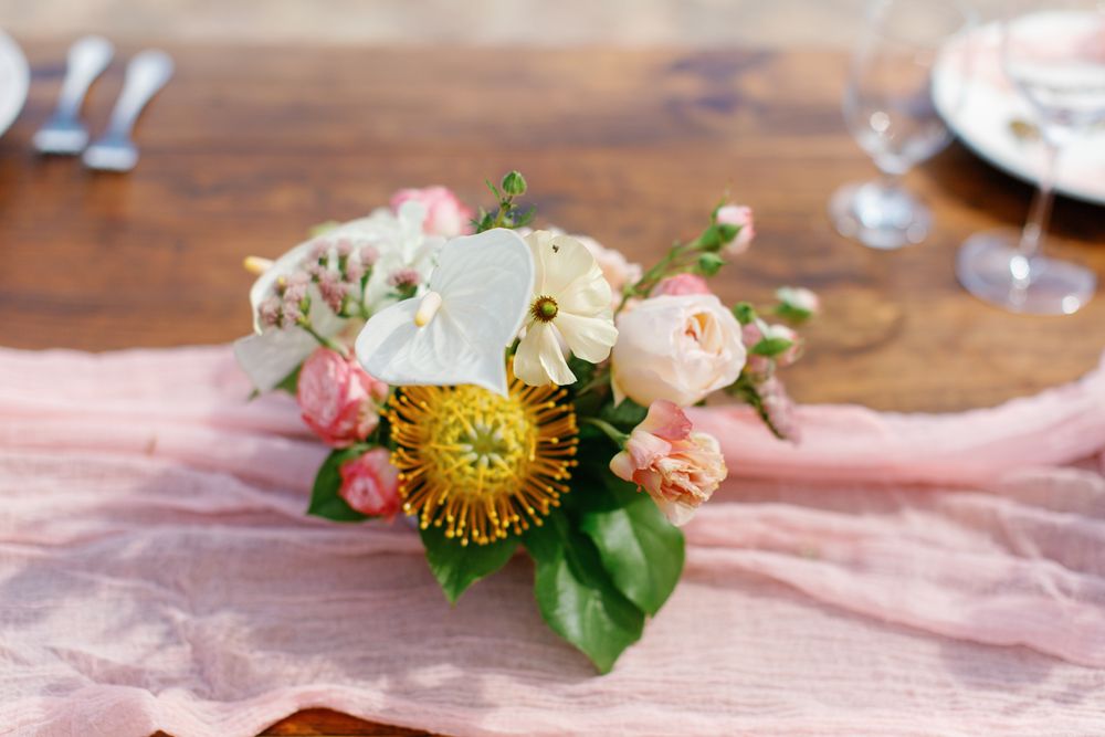 Small floral centerpiece with pink garden roses, yellow protea flowers and white blooms on a blush tablecloth.