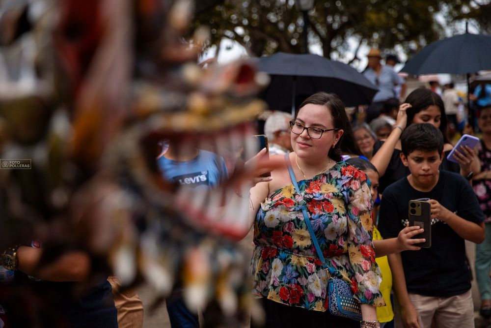 una chica toma una foto de las danzas de diablos durante el corpus christi