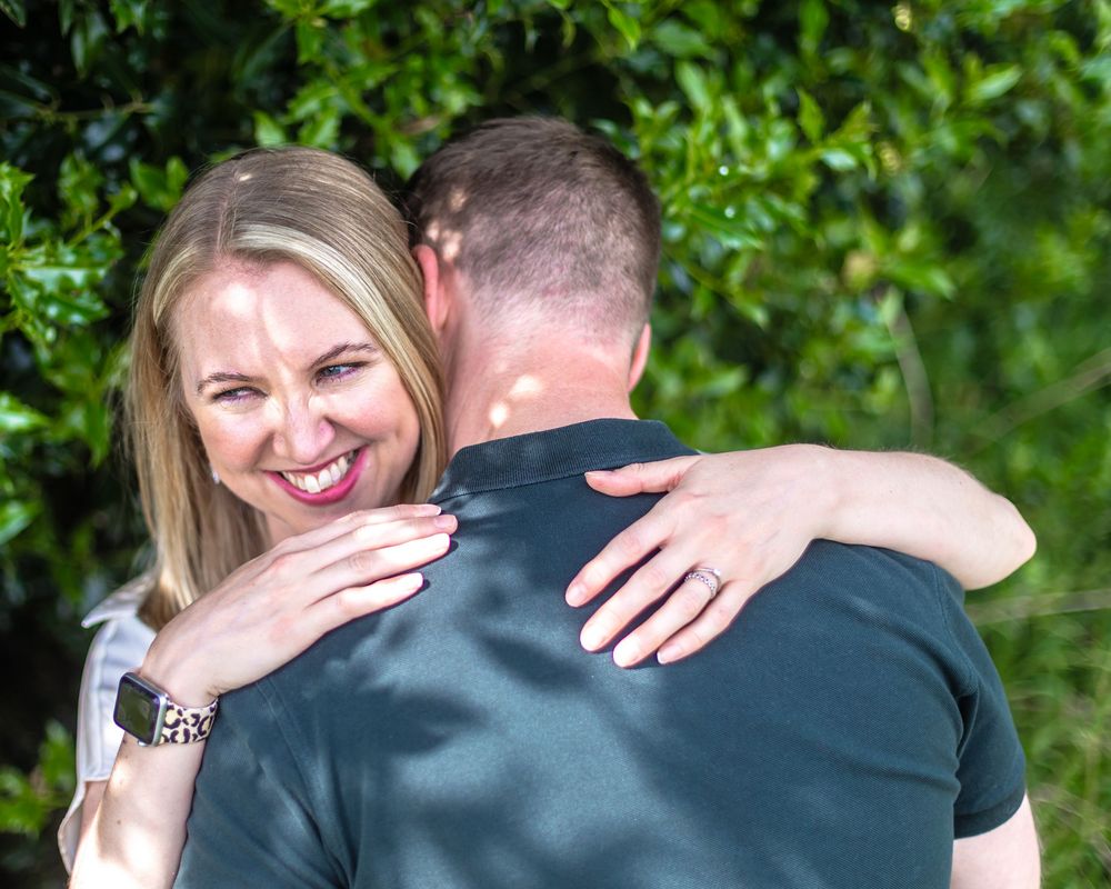 Two people embrace outdoors against a green foliage background on a sunny day, showing pure joy and happiness.