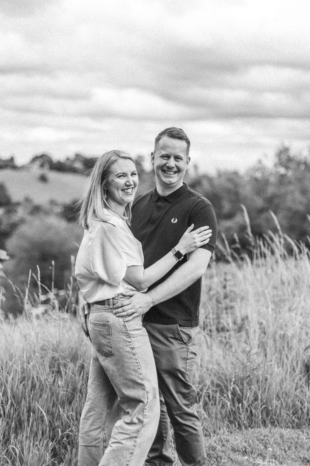 A couple shares intimate candid moments together in a grassy field under moody skies.