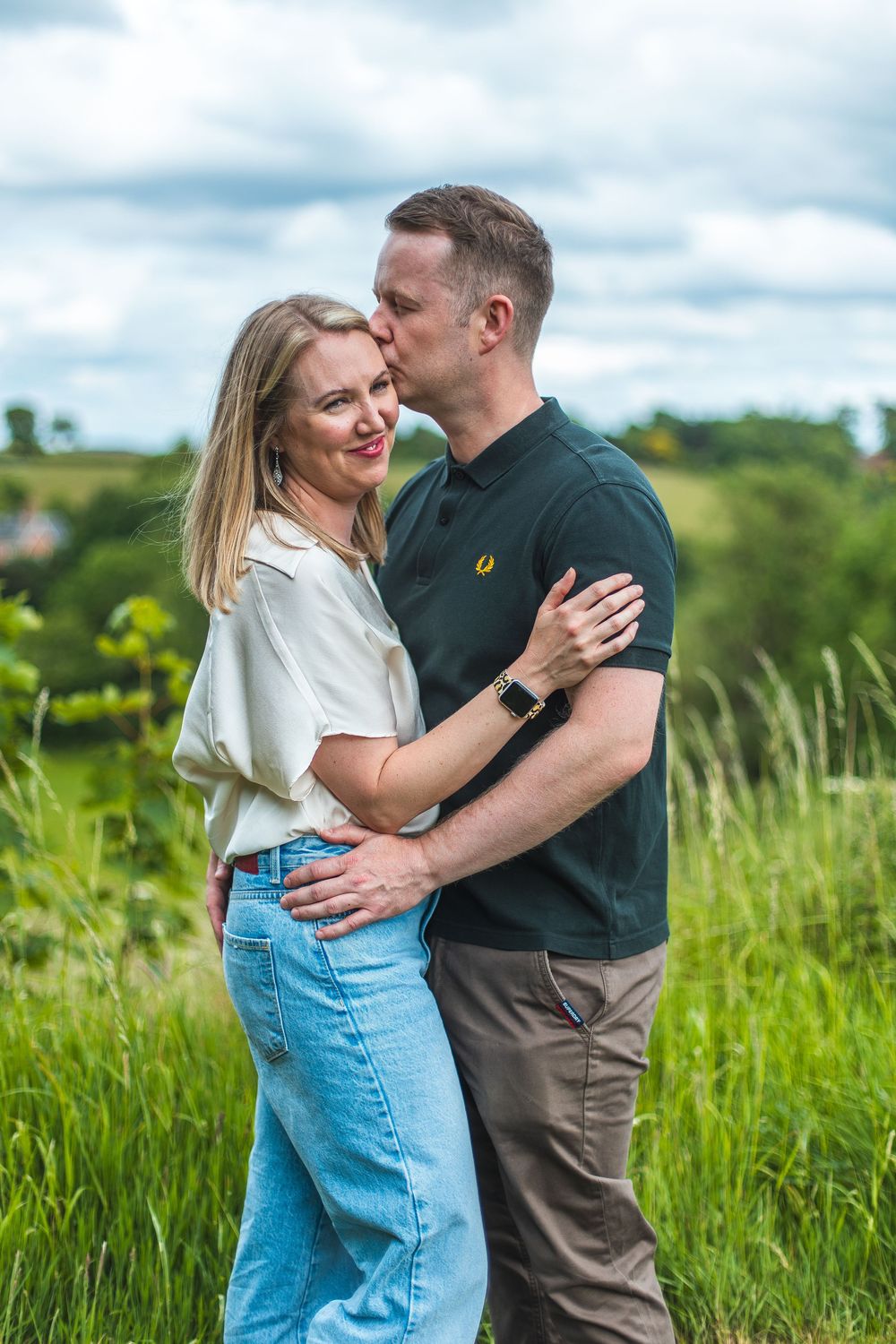 A couple embraces and laughs together in a sunny meadow with tall grass.