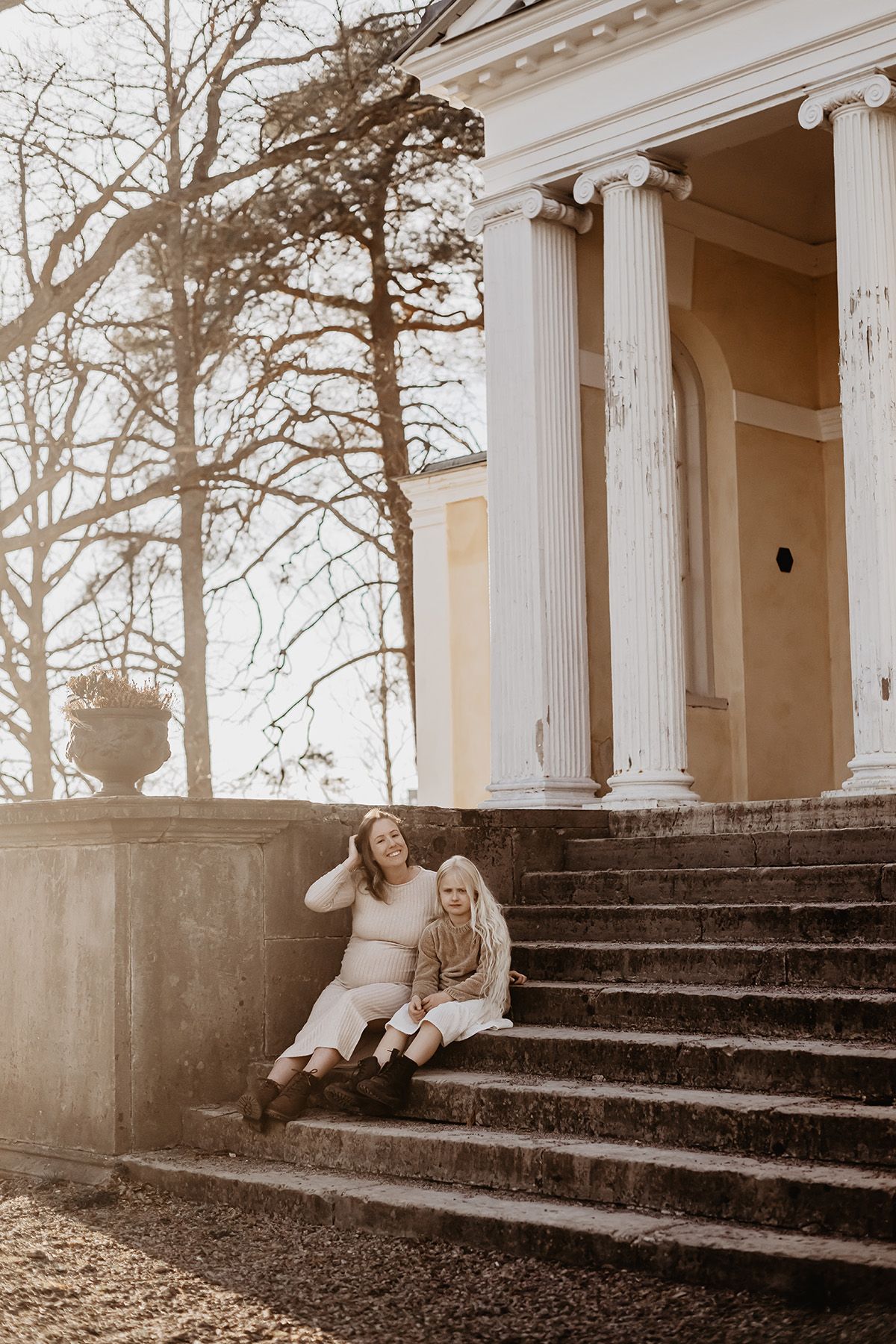 Gravidfotografering med mor och dotter i en stentrappa vid Lusthuset Lugnet i Finspång. Det är vackert motljus och miljön rustik.