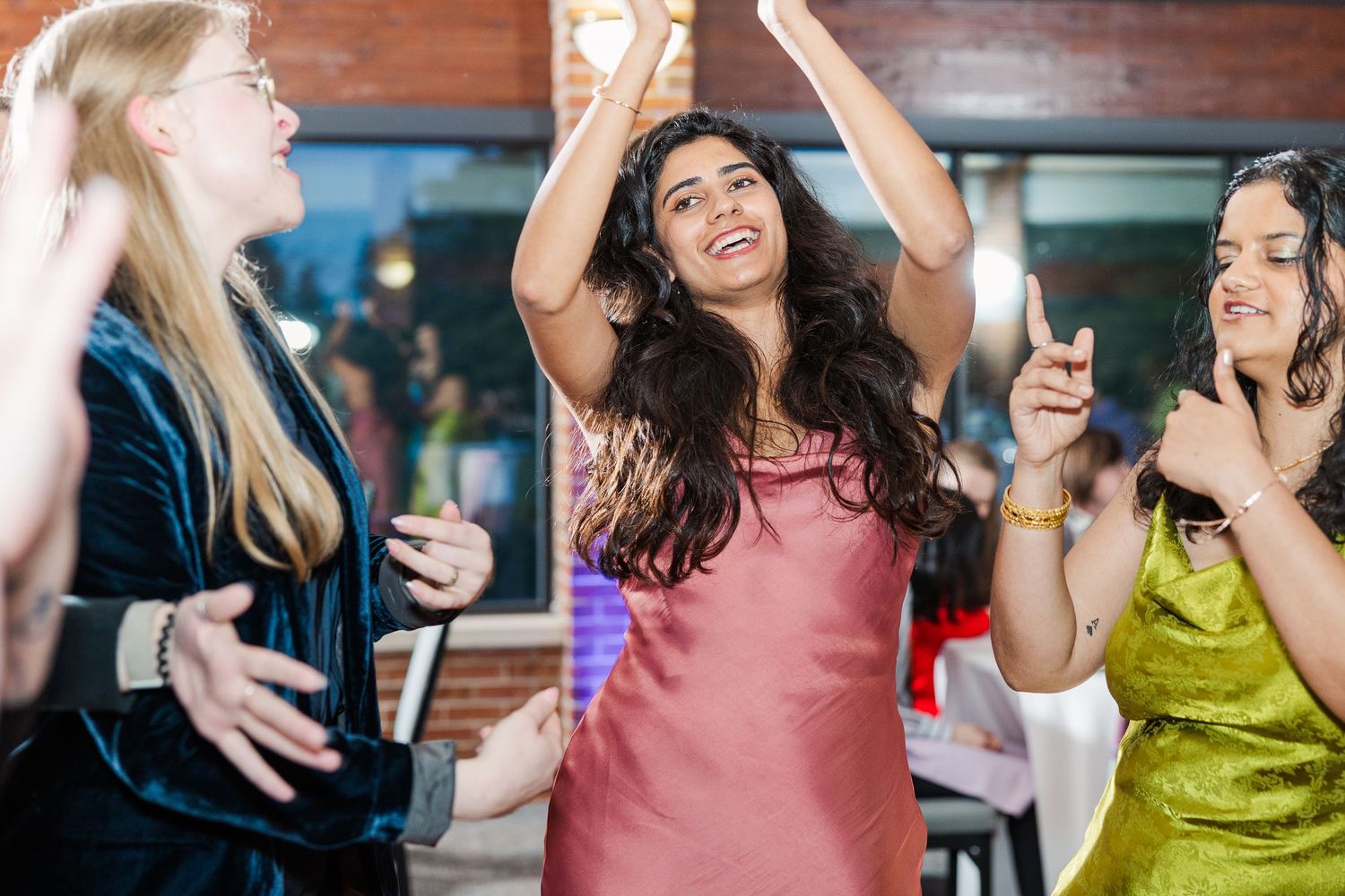 Three friends dance and celebrate with enthusiasm at a social gathering, wearing colorful party dresses.