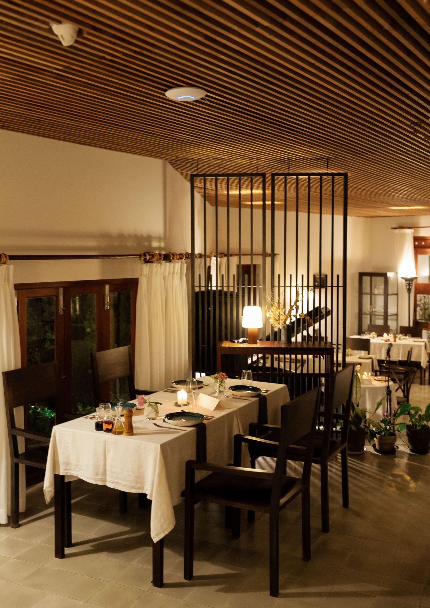 Elegant restaurant interior with wooden ceiling, white tablecloths, and modern black metal dividers creating an intimate dining space.