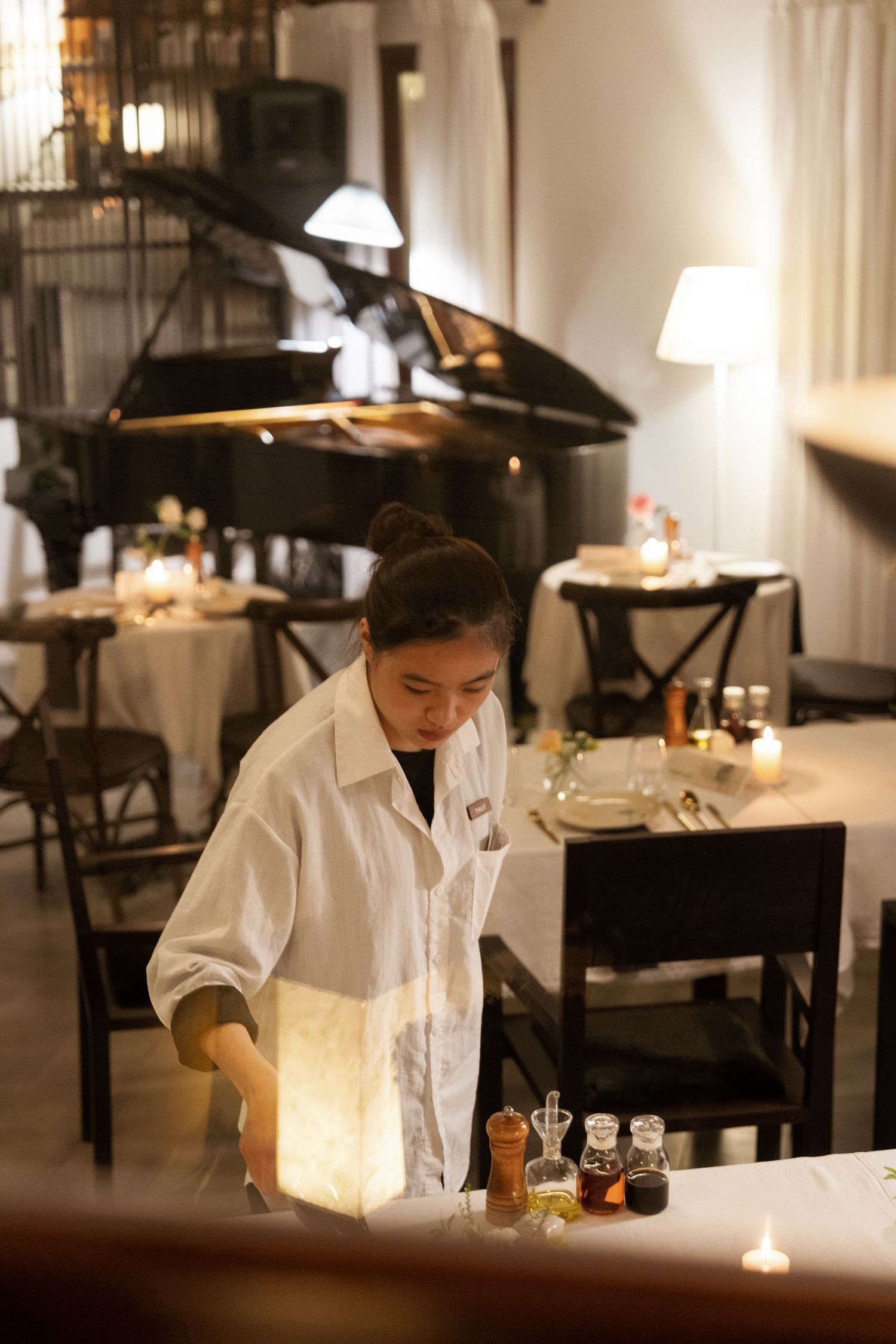 Restaurant server in white shirt works at candlelit tables in dimly lit upscale dining room.