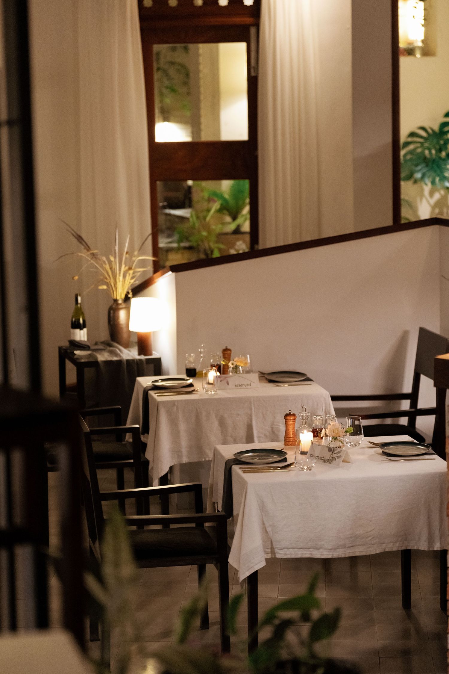 Intimate restaurant interior with elegantly set tables draped in white linens, soft lighting and modern minimalist decor.
