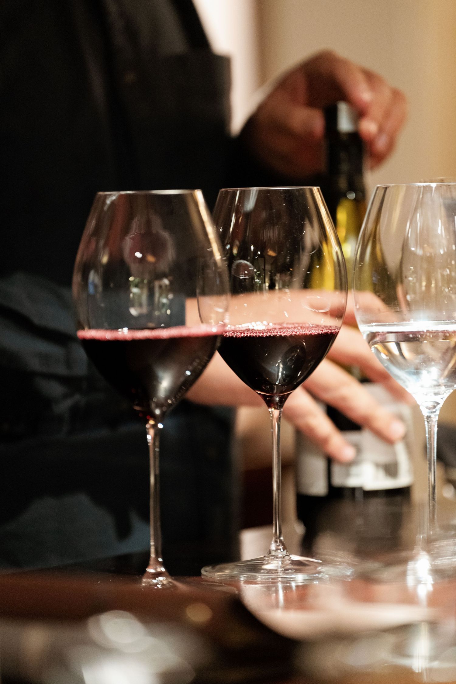 Several wine glasses filled with red wine and white wine sit on a wooden table during a wine tasting service.