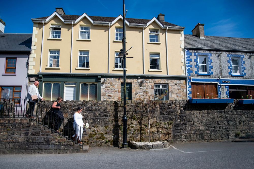 Row of traditional stone houses with white trim along a Welsh village street against bright blue sky.