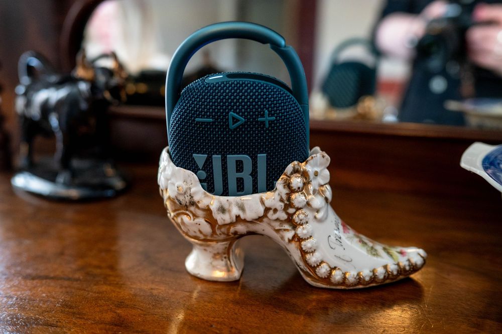 A JBL portable speaker sits atop an ornate vintage white ceramic boot planter on a wooden surface.